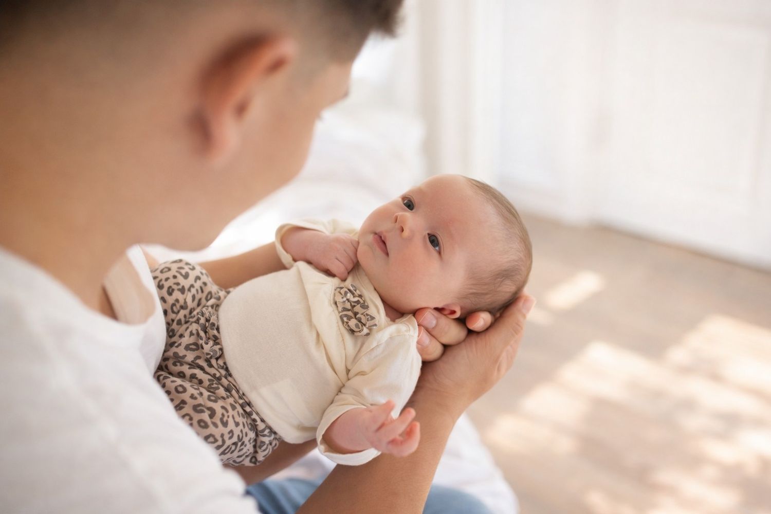 A parent lovingly holds and interacts with a small baby in a bright, sunlit room.
