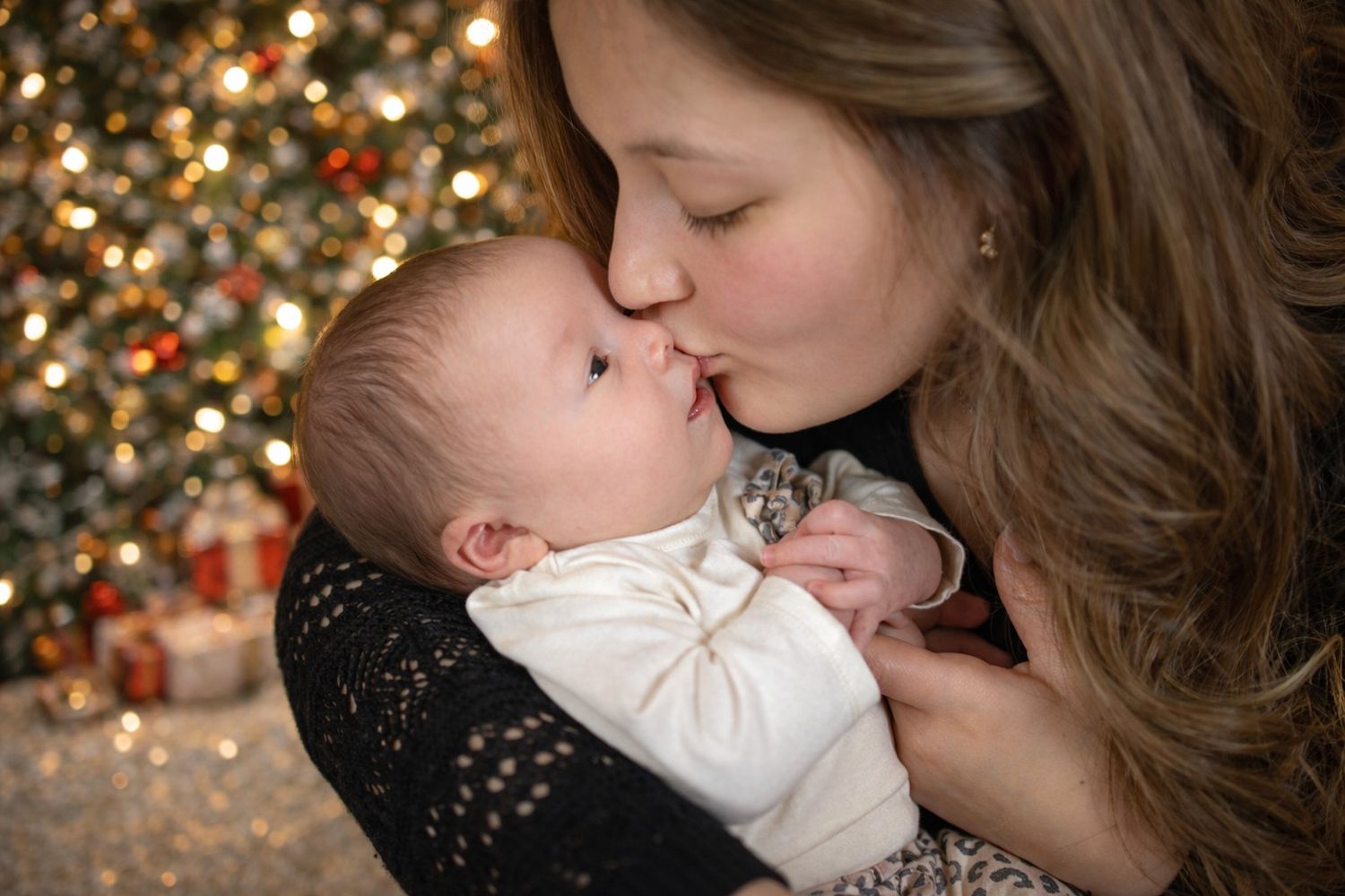 A tender moment captured in front of a twinkling Christmas tree with warm bokeh lights in the background.