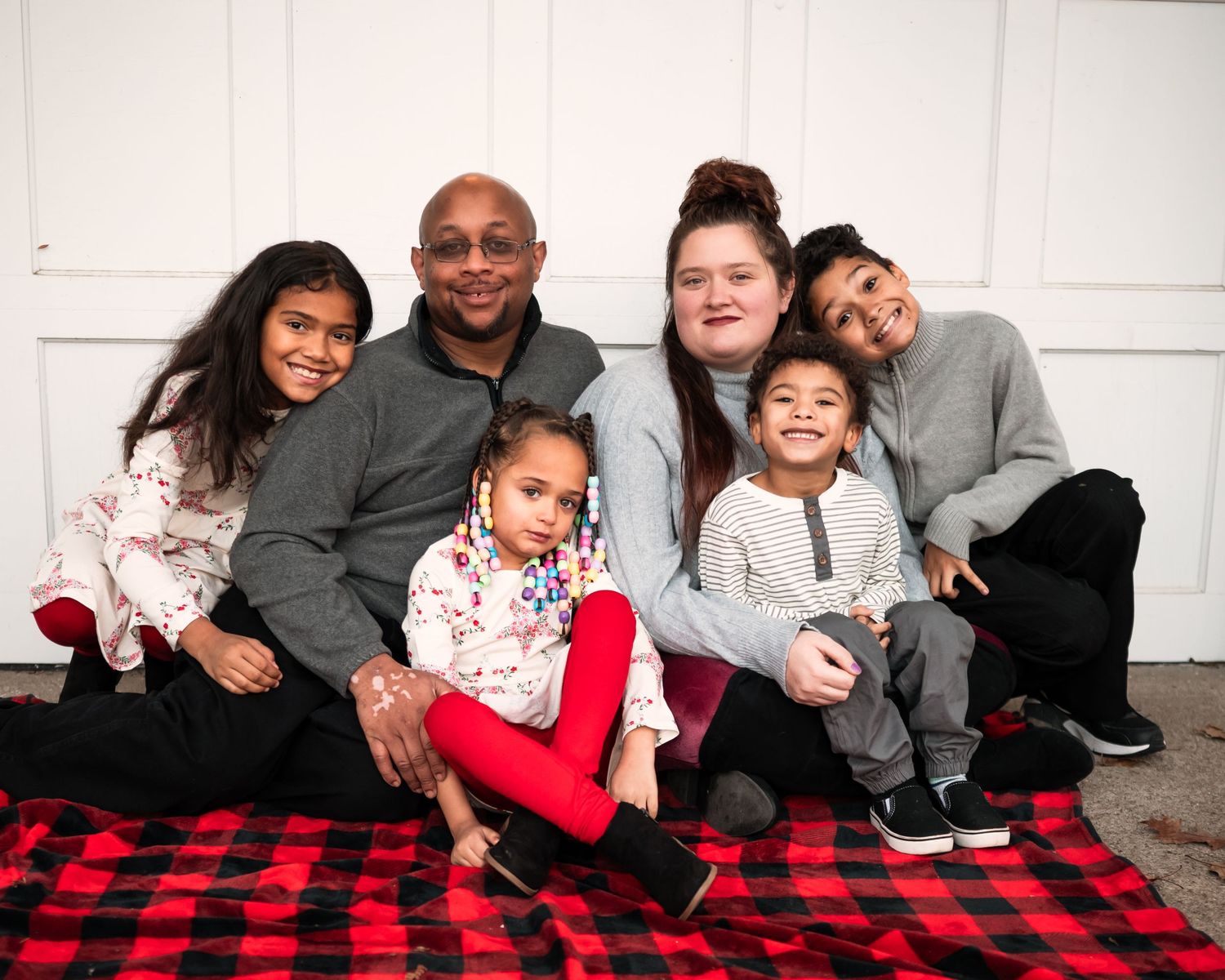 A series of family photos showing people sitting together on a red and black buffalo plaid blanket.