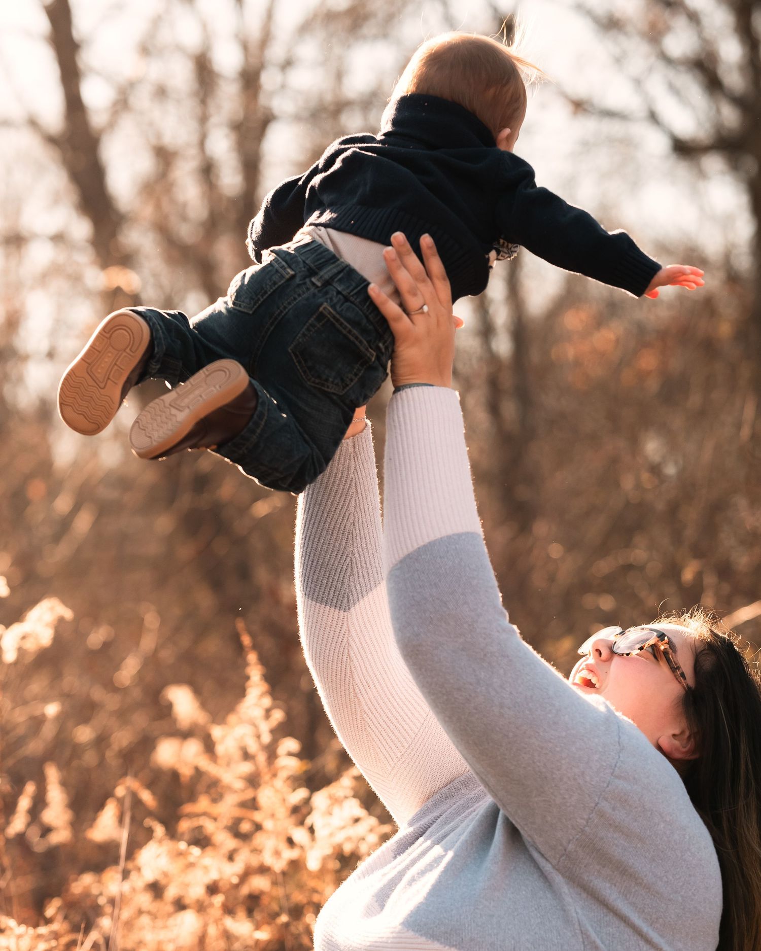 A parent lifts and plays with a small child in a golden autumn field during sunset.