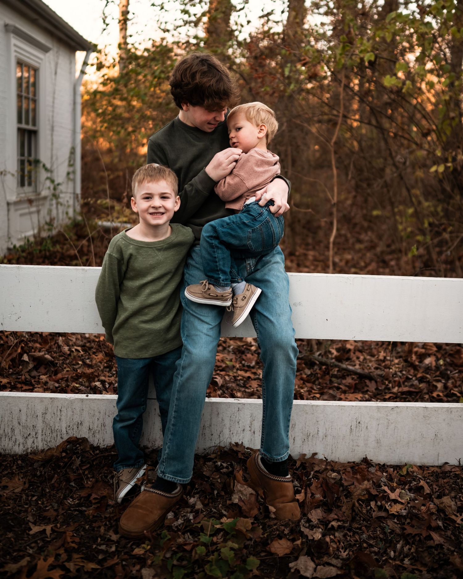 Two young boys in green shirts and jeans play together on a white fence at sunset.
