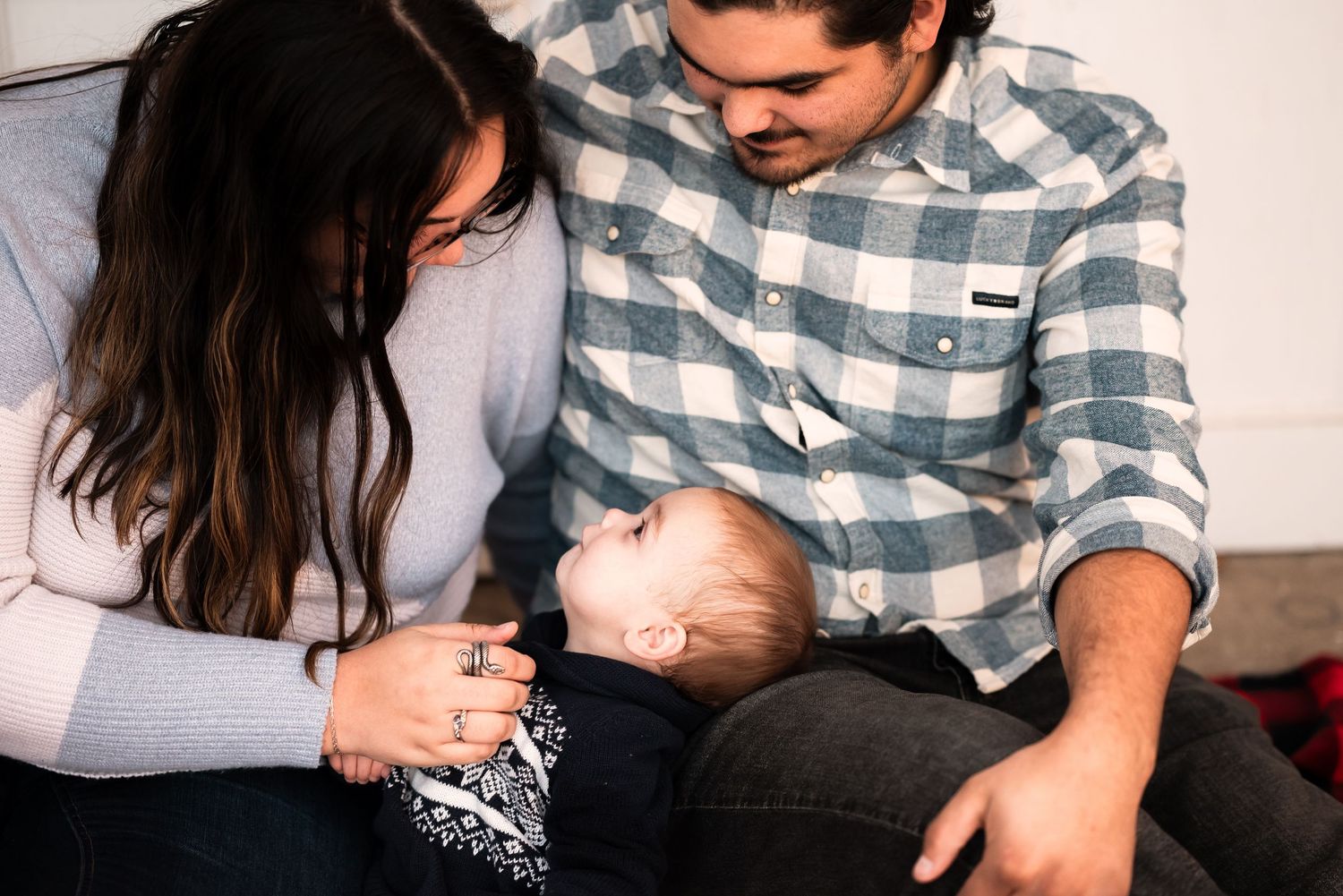 A couple in a plaid shirt and gray sweater share tender moments while holding their newborn baby in a series of photos.