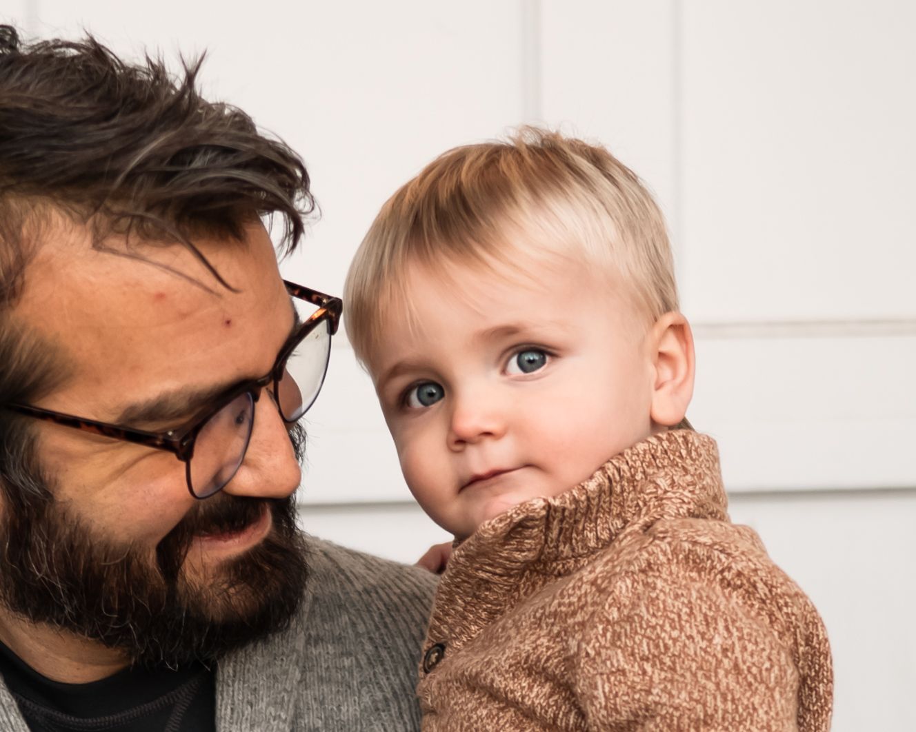 A series of tender moments between a bearded adult and small child wearing a knit sweater.