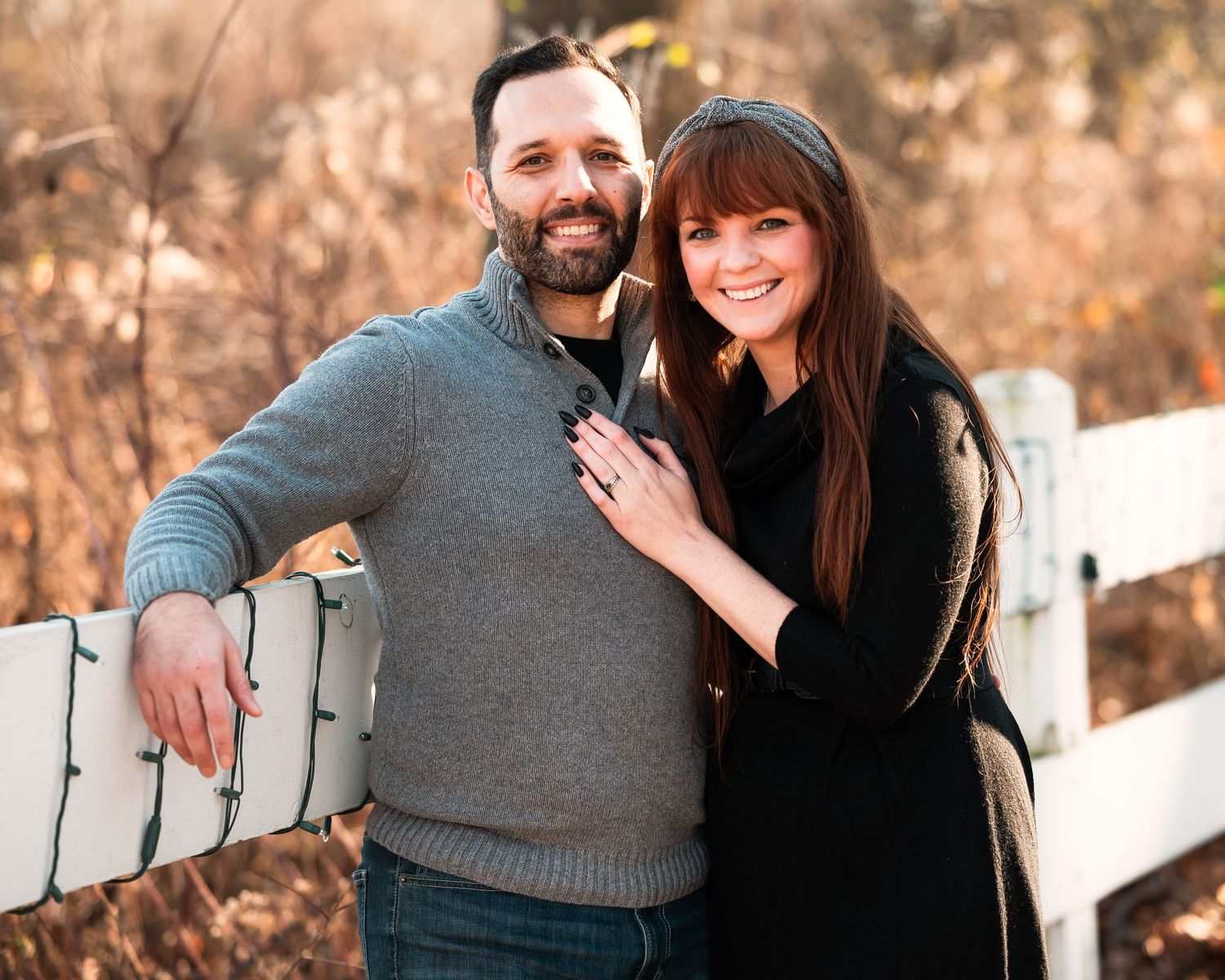 A couple shares romantic moments along a white fence during a fall sunset photo session.