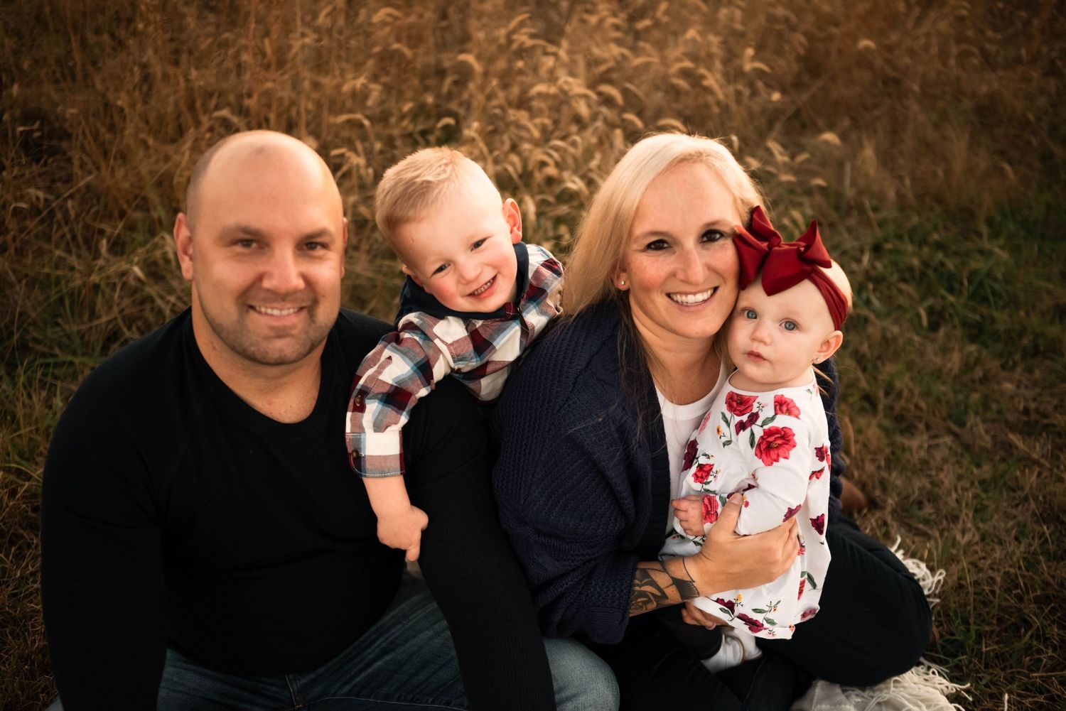 Professional family portrait in rustic field setting with warm lighting.