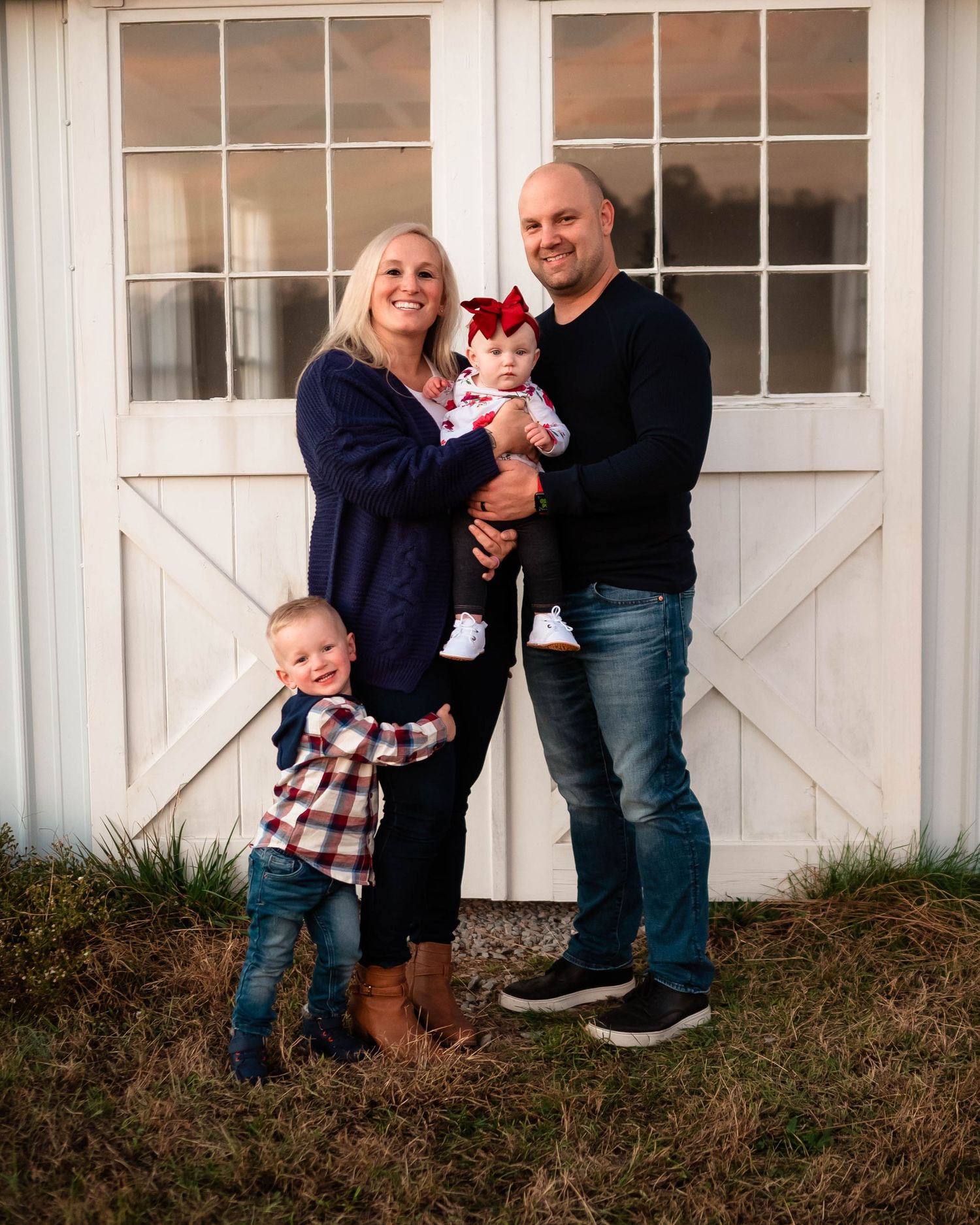 Family portrait session in front of a white barn showing playful interactions.