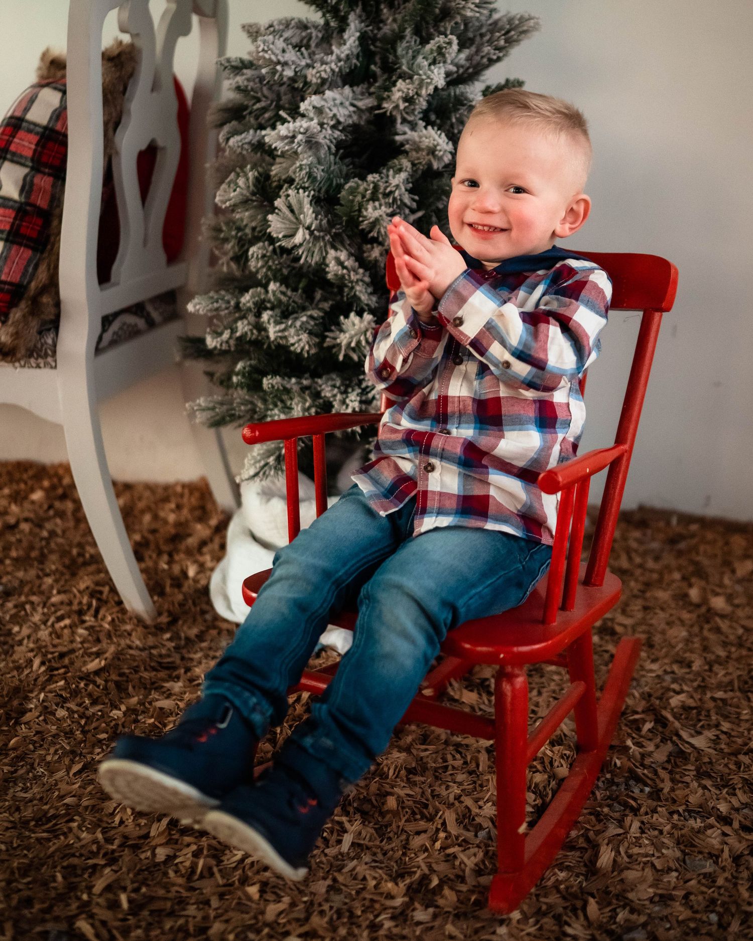 Child sitting in red rocking chair next to Christmas decorations showing happy expressions.