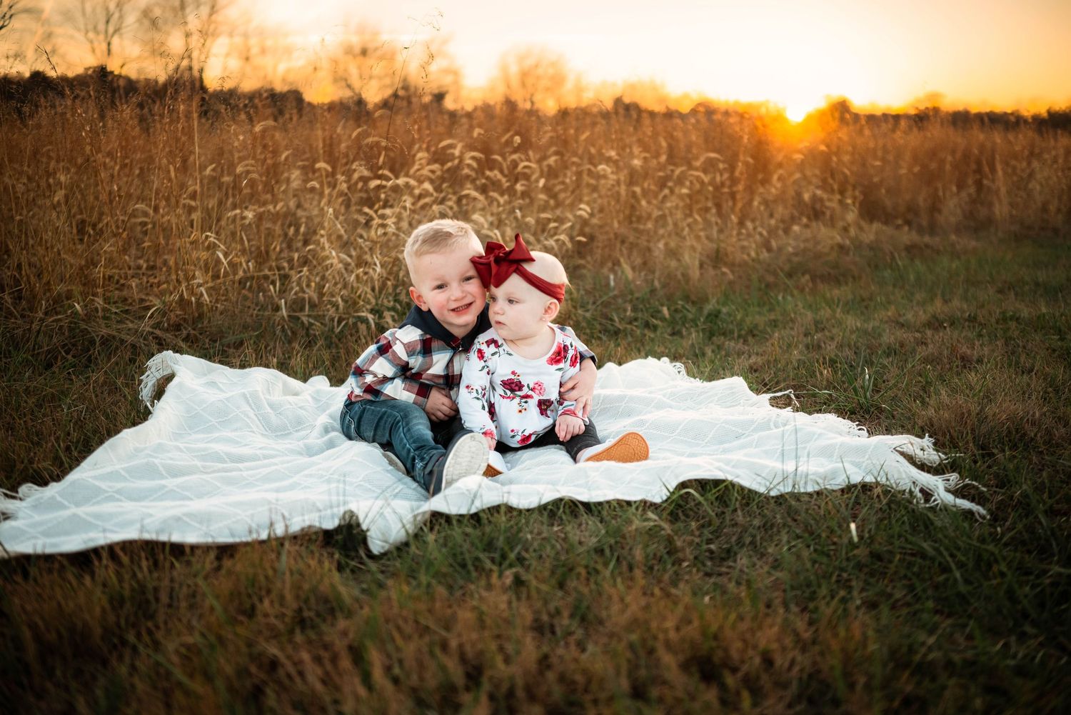 Family sitting on white blanket in field during sunset photo session.
