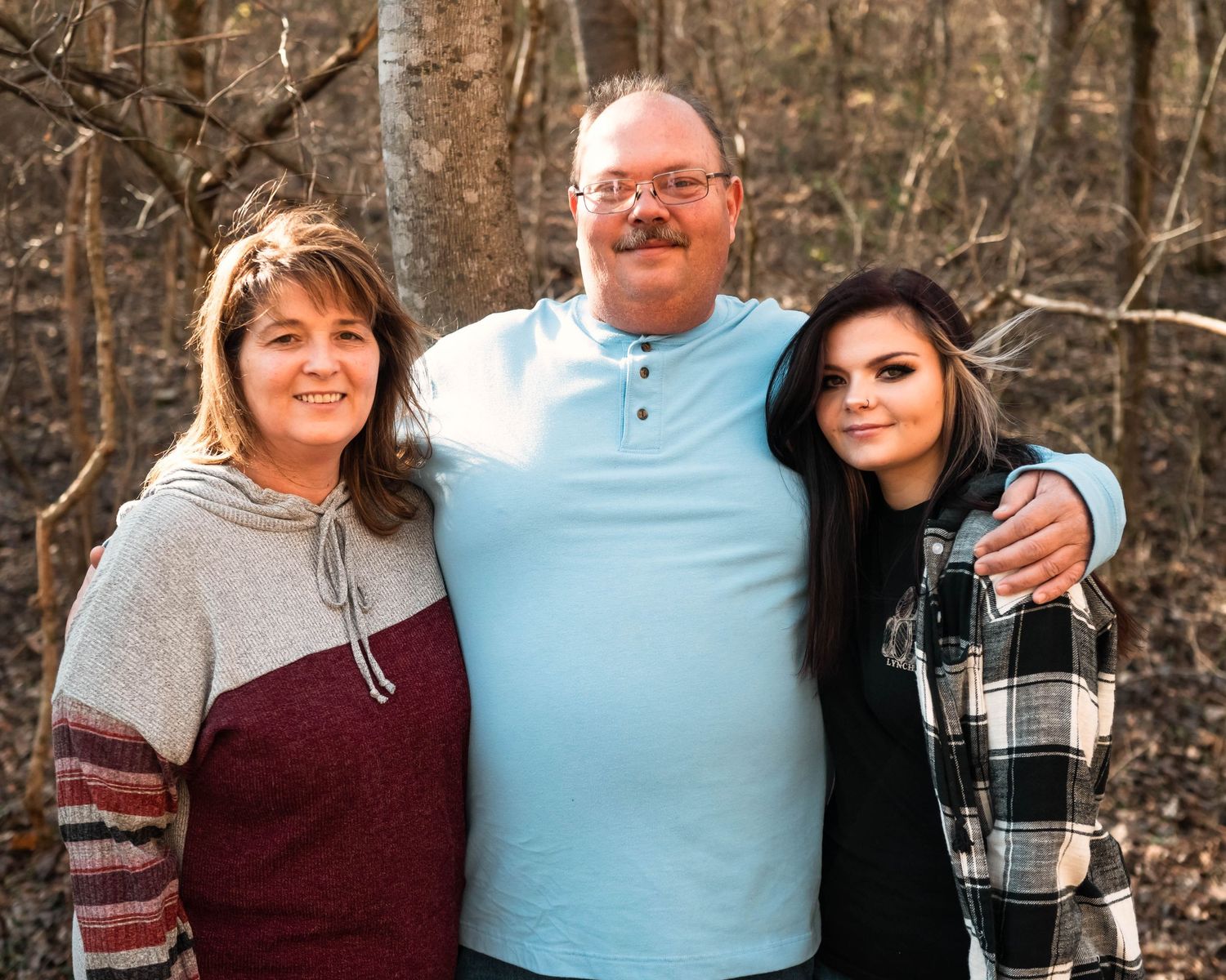 Family members pose together in casual winter attire against a wooded background.