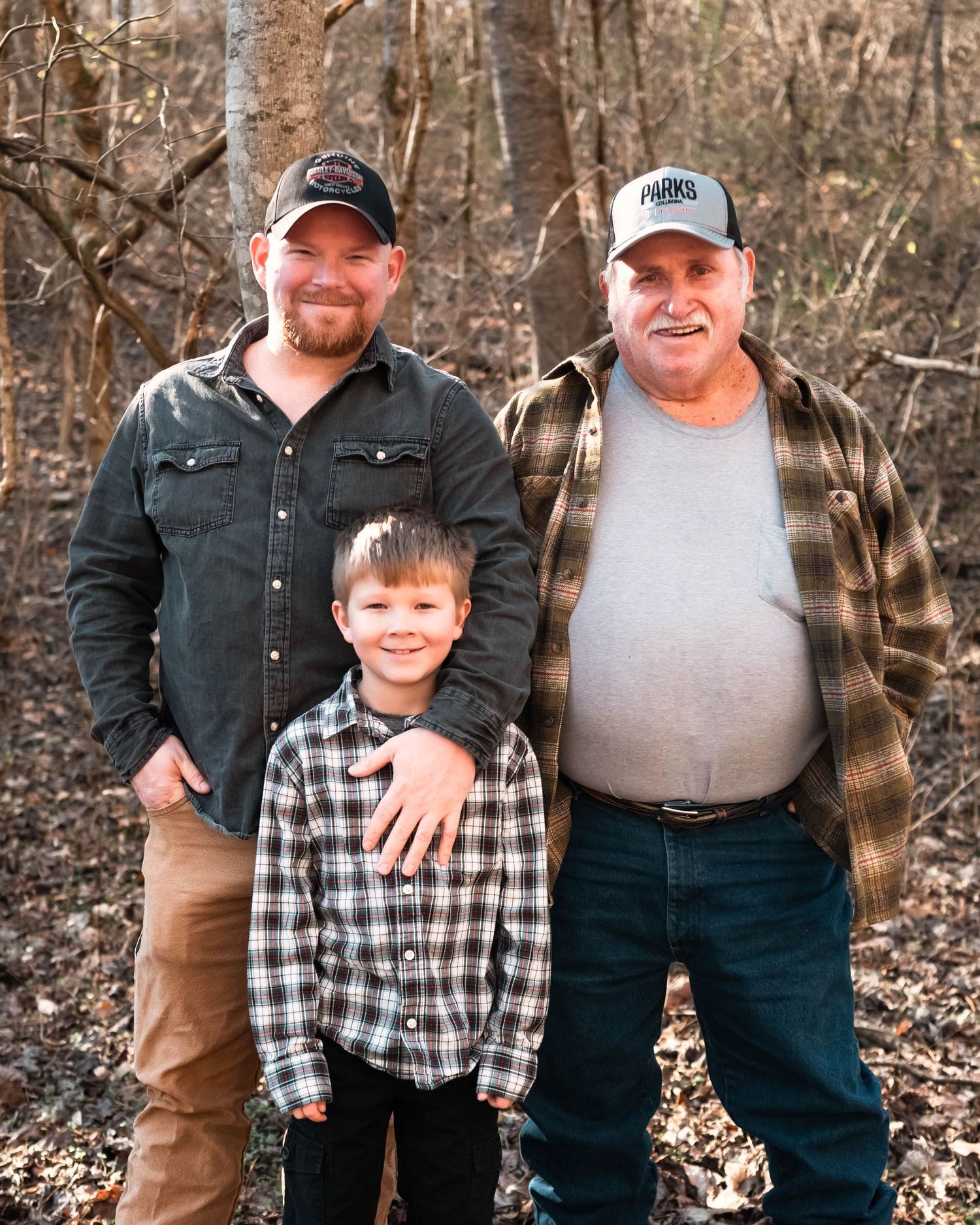 Multi-generational family members stand together for outdoor portraits in casual clothing.