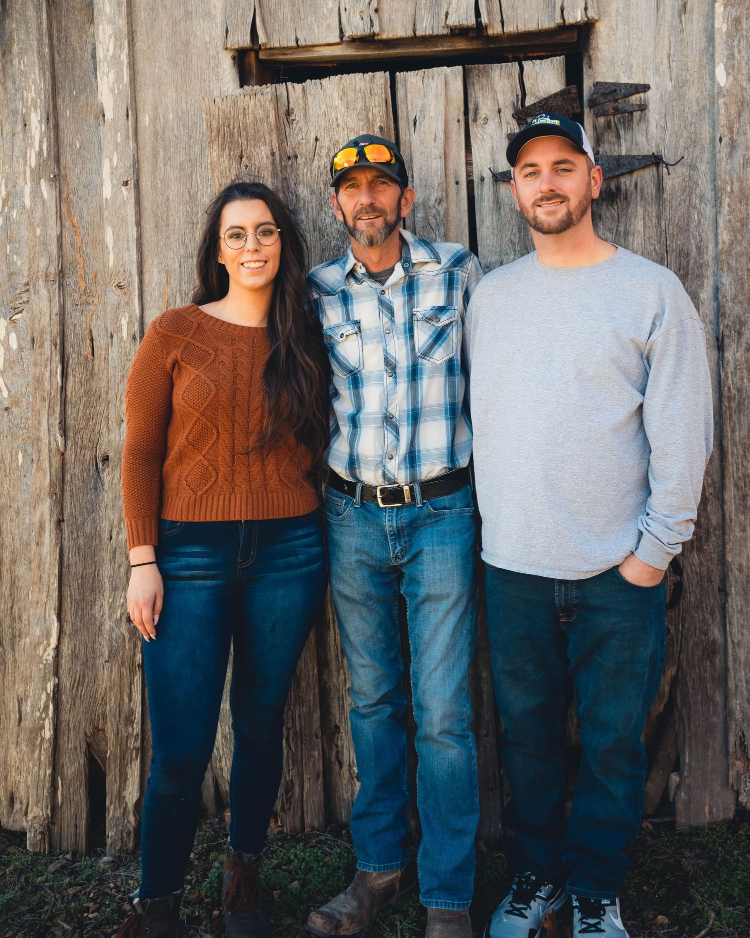 Family group poses against weathered wooden barn wall in coordinated casual outfits.