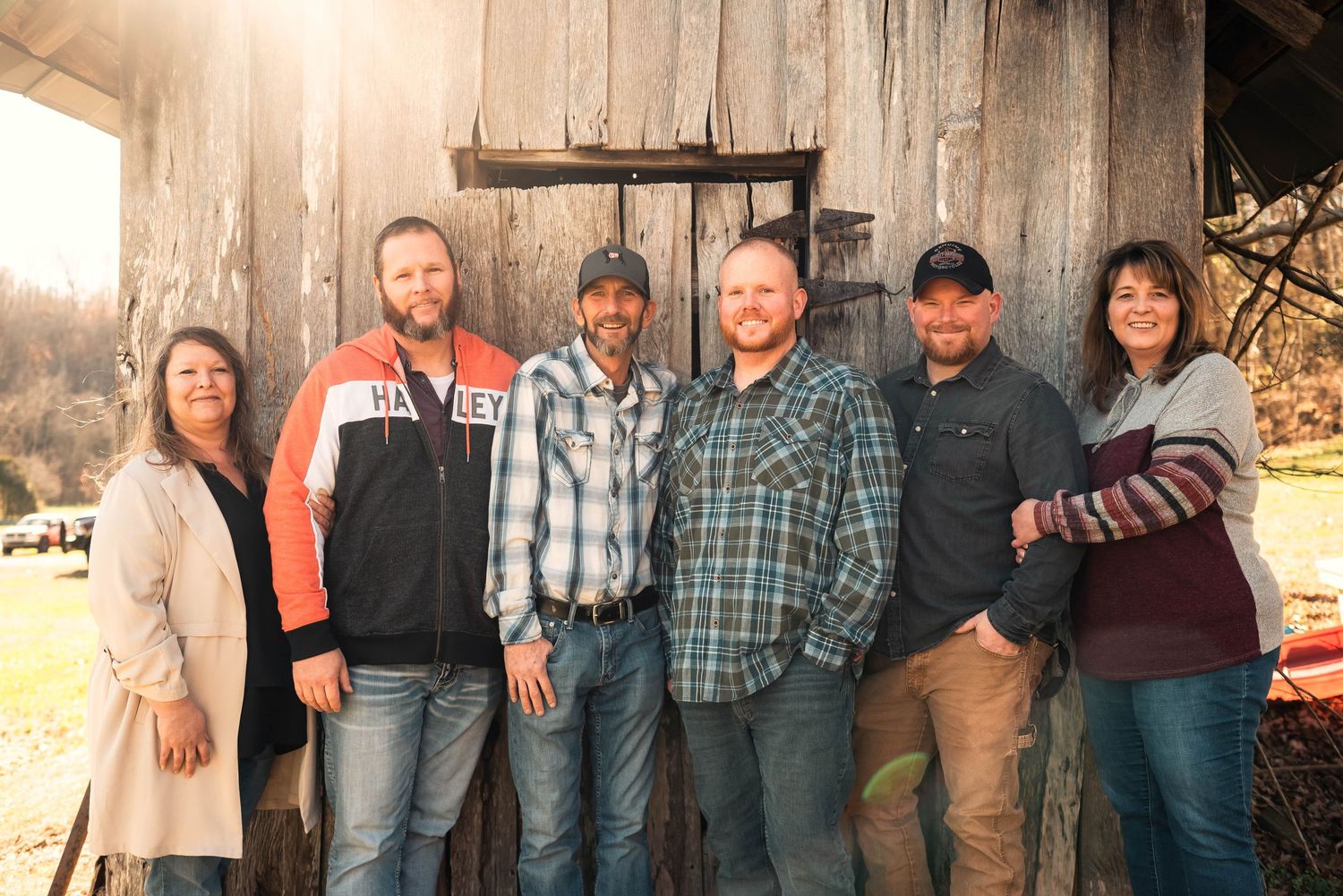Group photo of six people standing together in front of a rustic barn at sunset.