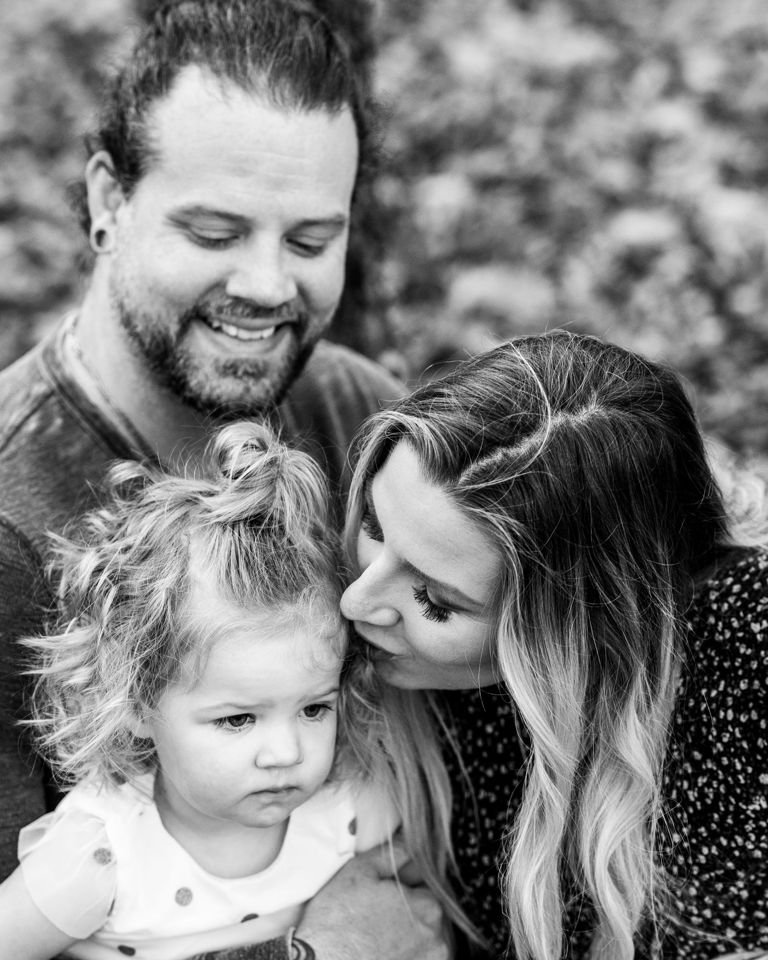 Black and white family portrait showing intimate moments between parents and child outdoors.