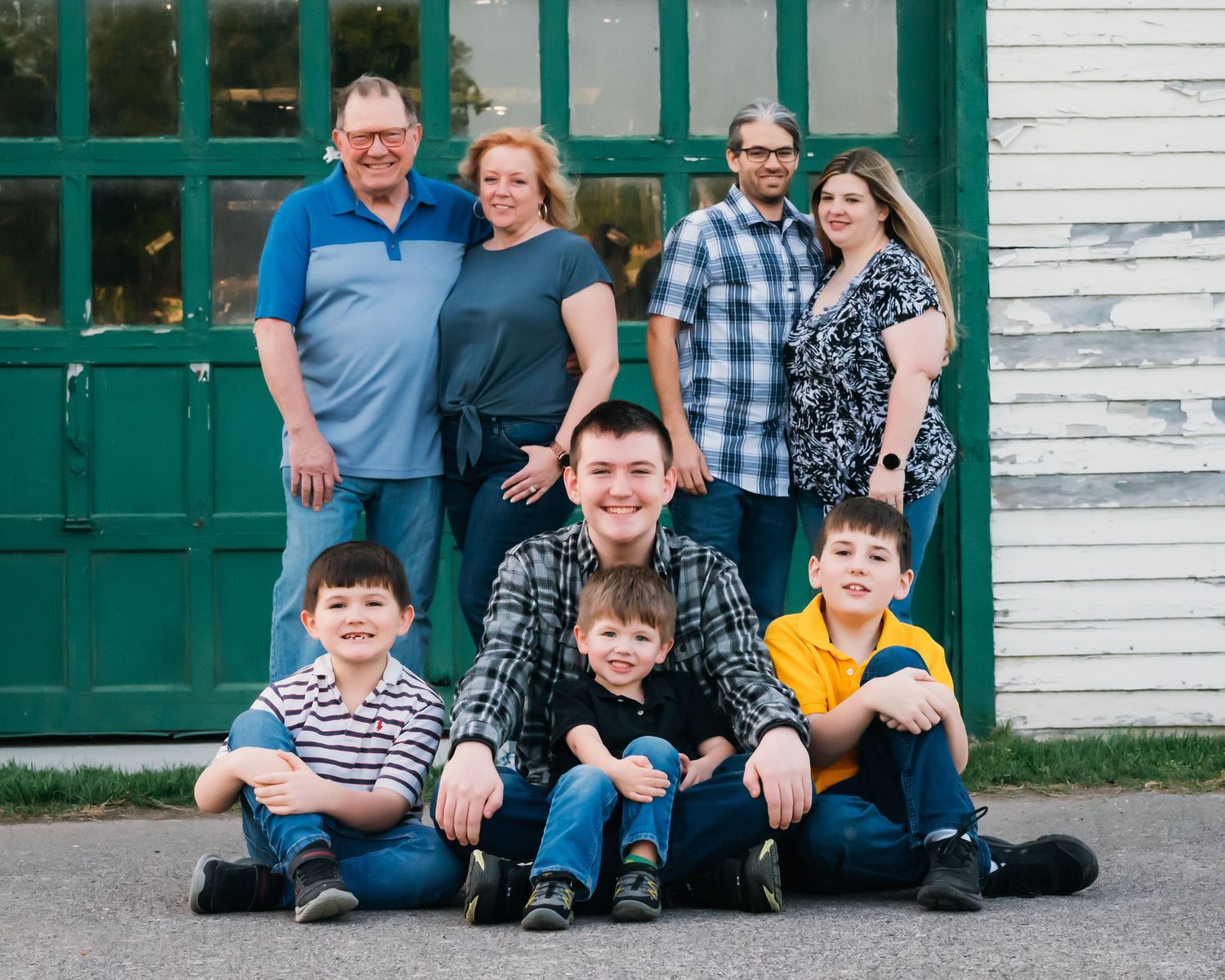 Multi-generational group poses in front of historic white building with green doors.