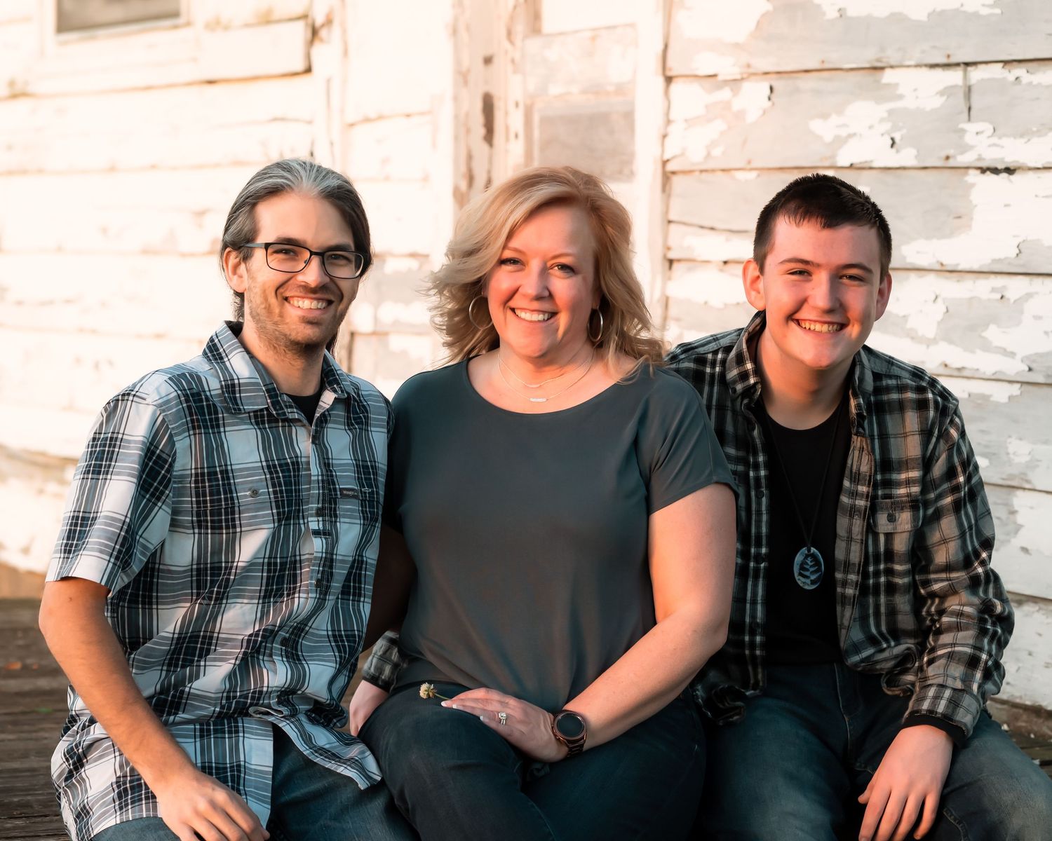 Family sitting together on steps with white wood siding and green trim in background.