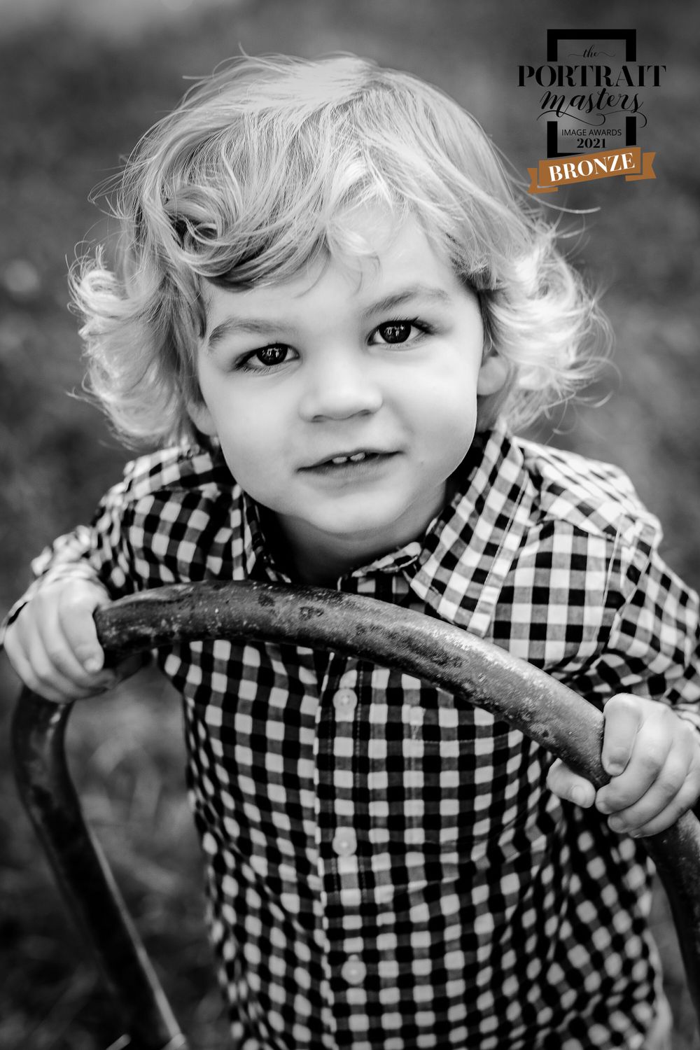 Child in black and white checkered shirt playing with a stick outdoors.
