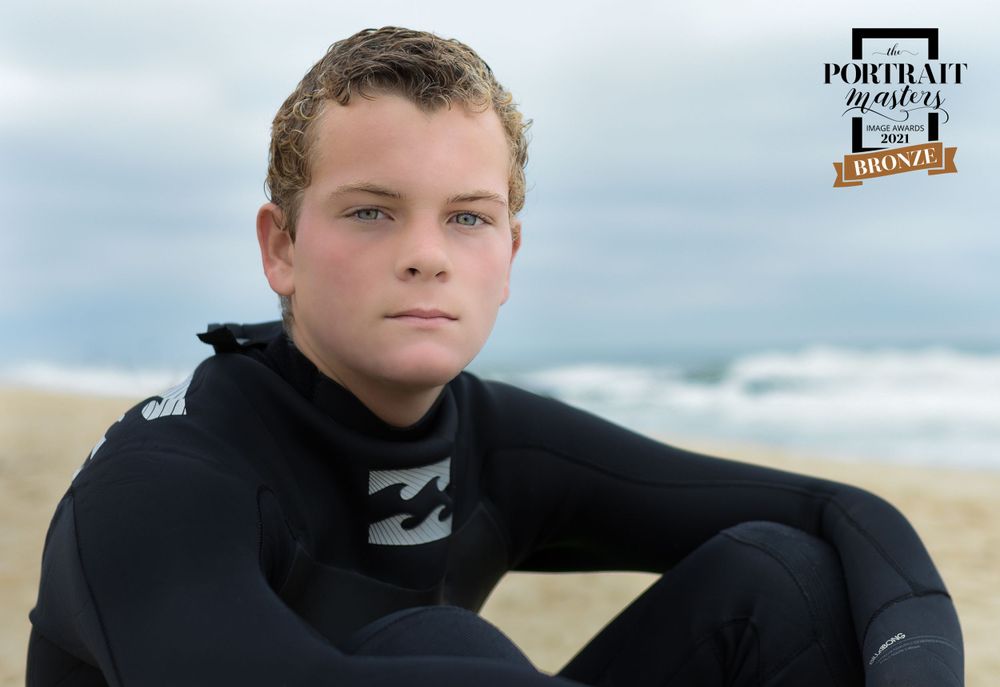 Young person in wetsuit sitting on beach during overcast day.