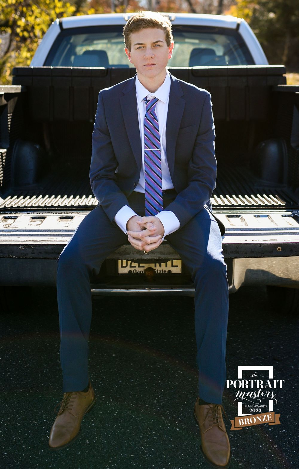 Person in navy suit sitting on truck bed outdoors.