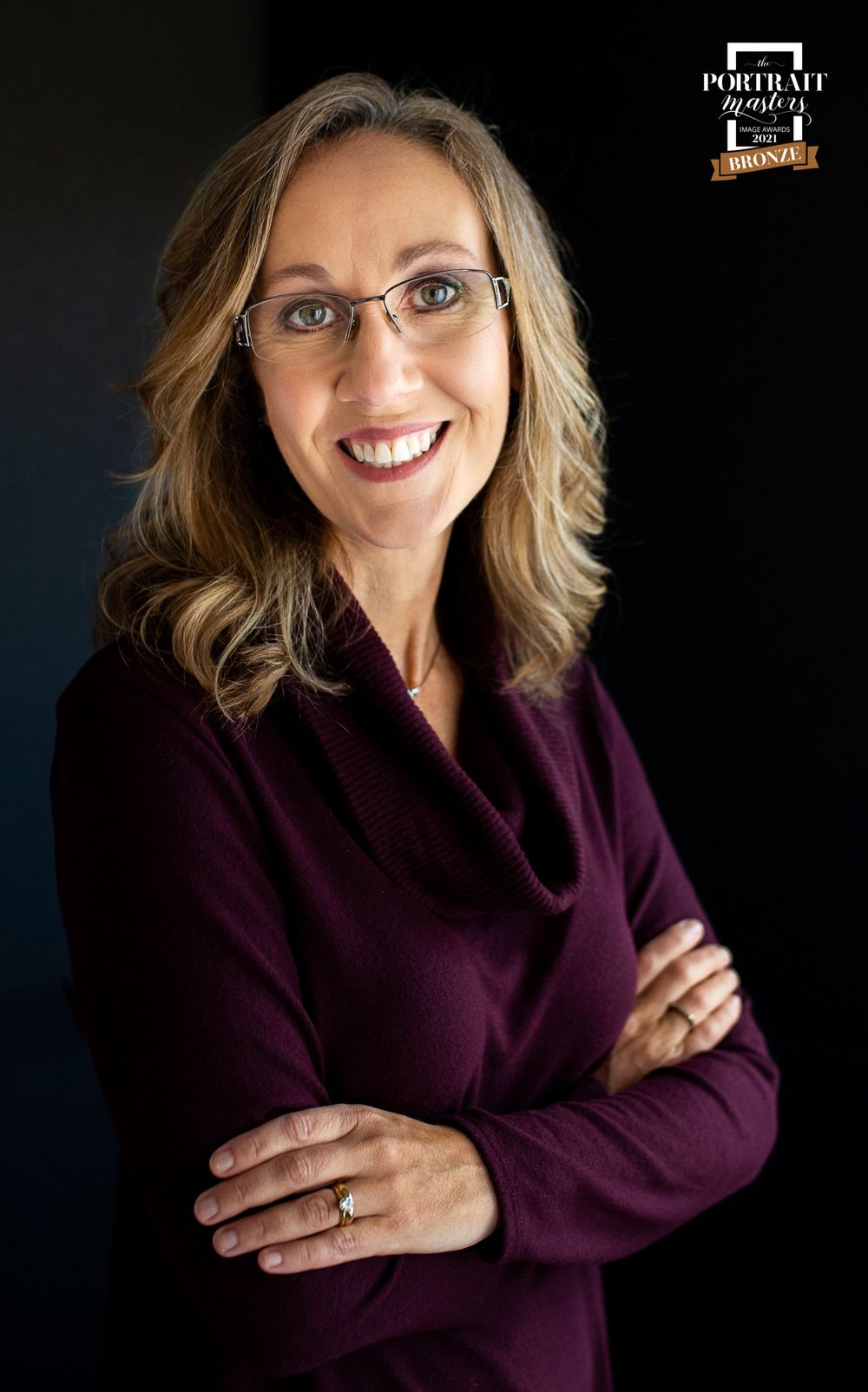 Professional headshot against dark background showing burgundy sweater and glasses.