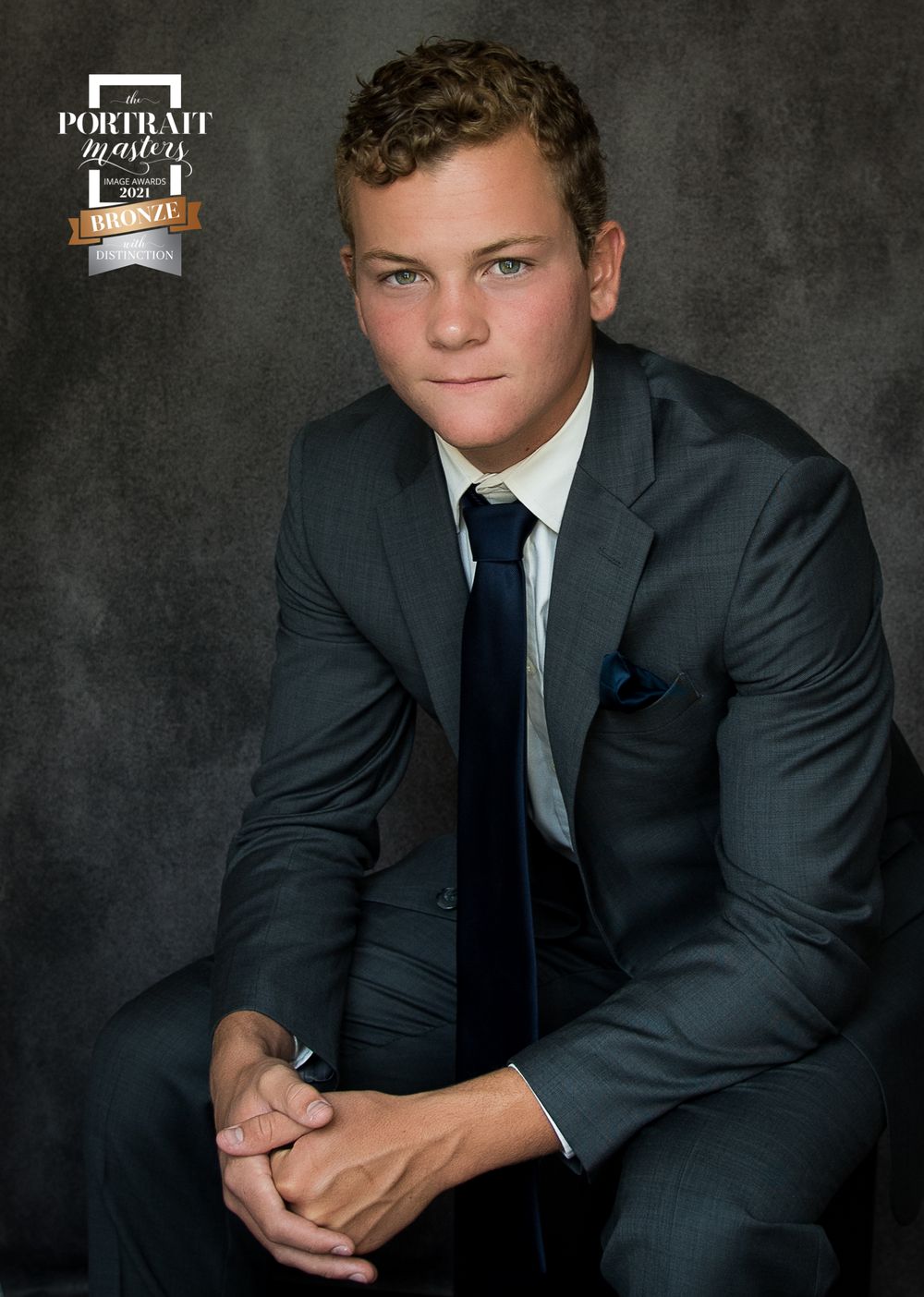 Professional studio portrait in dark suit and tie against gray backdrop.