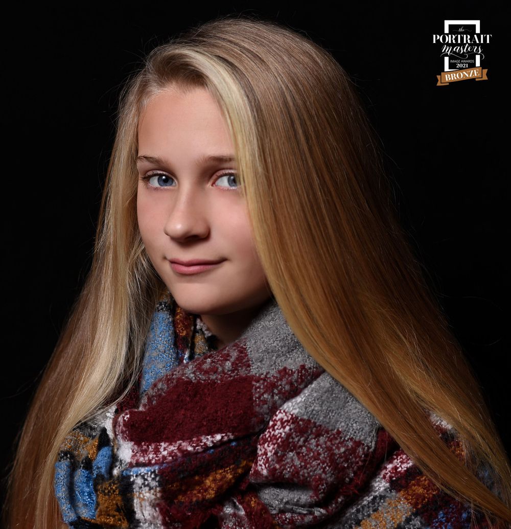 Portrait featuring long blonde hair and patterned winter scarf against black background.