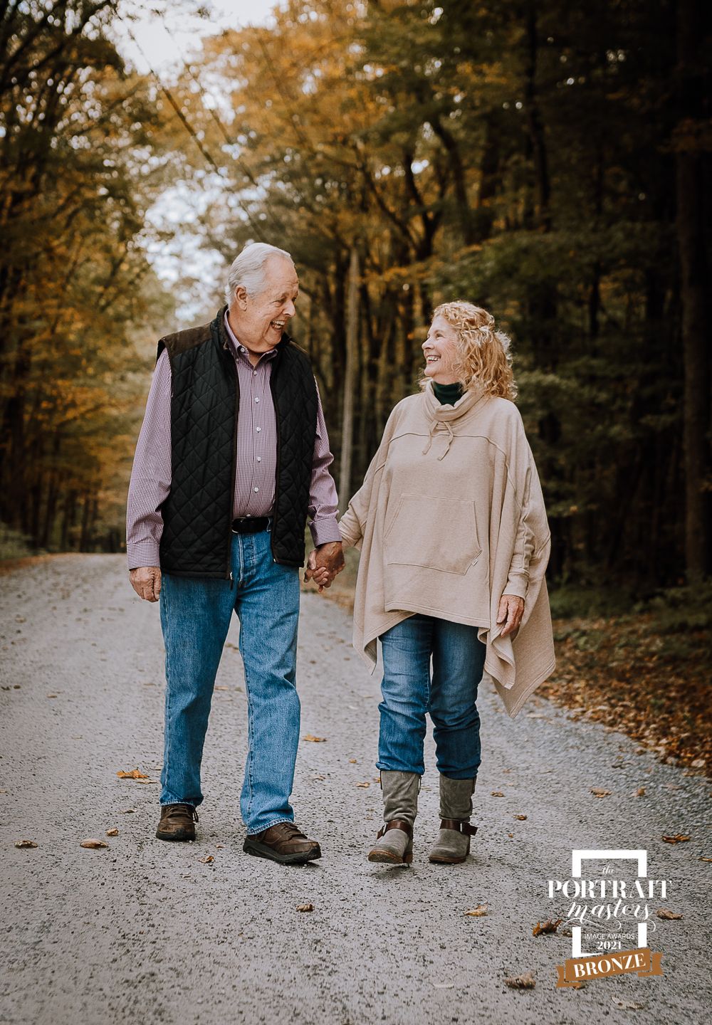 An elderly couple walking together on a tree-lined path during autumn.