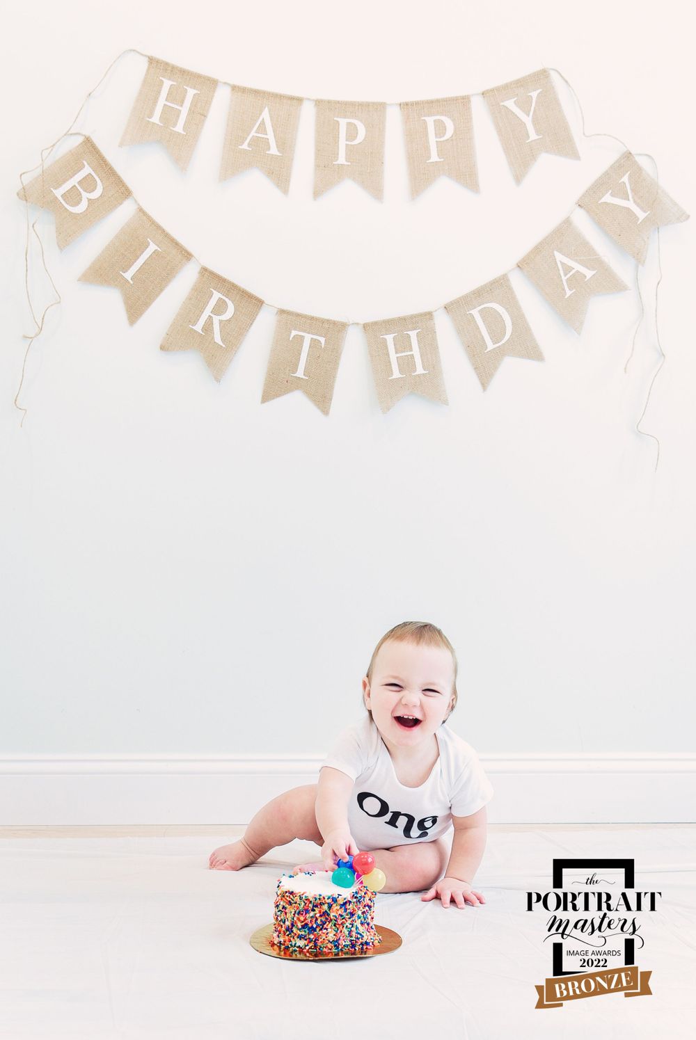 Baby celebrating first birthday with cake and banner decorations.