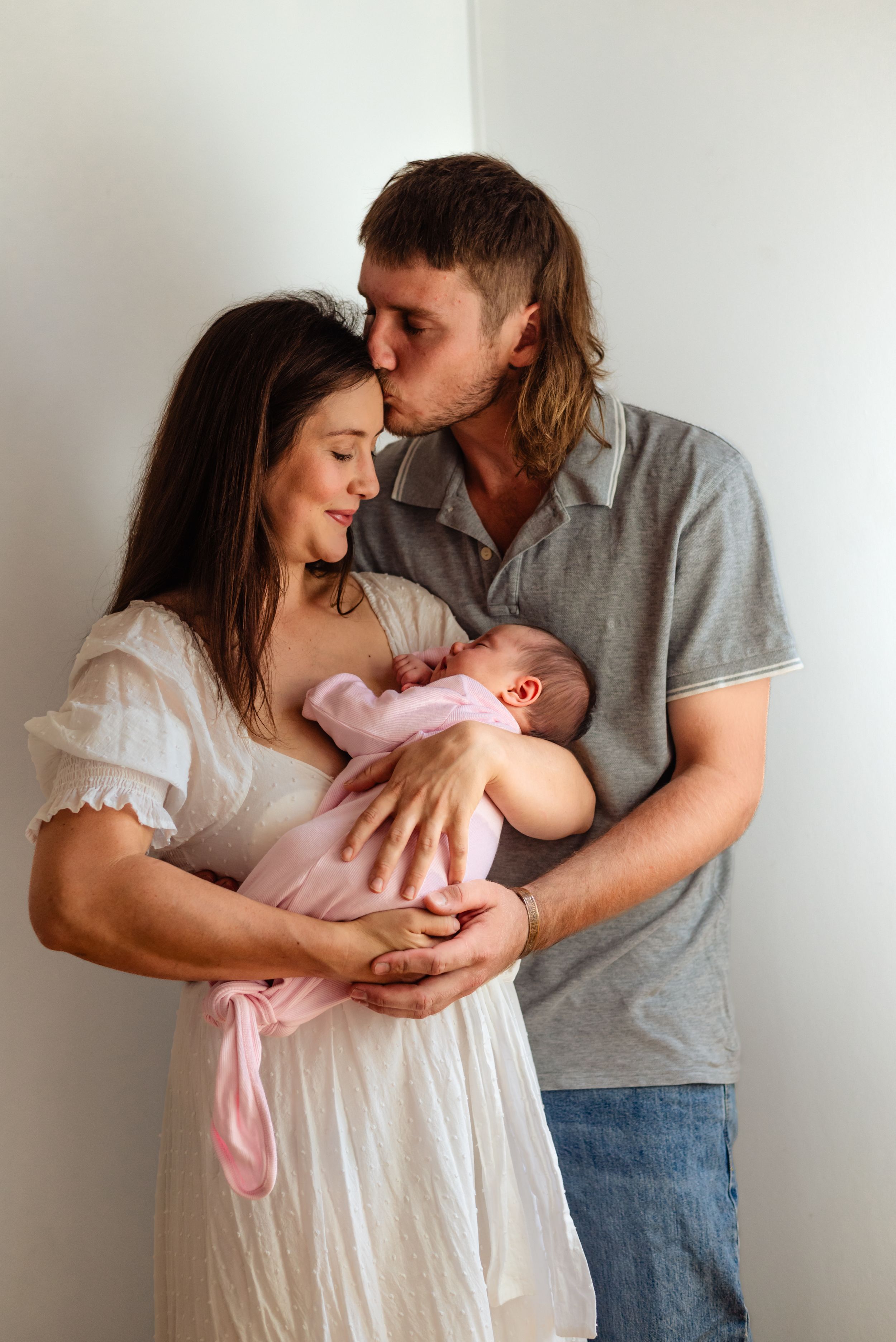 A loving couple in casual attire shares tender moments with their newborn baby in a series of intimate family portraits.