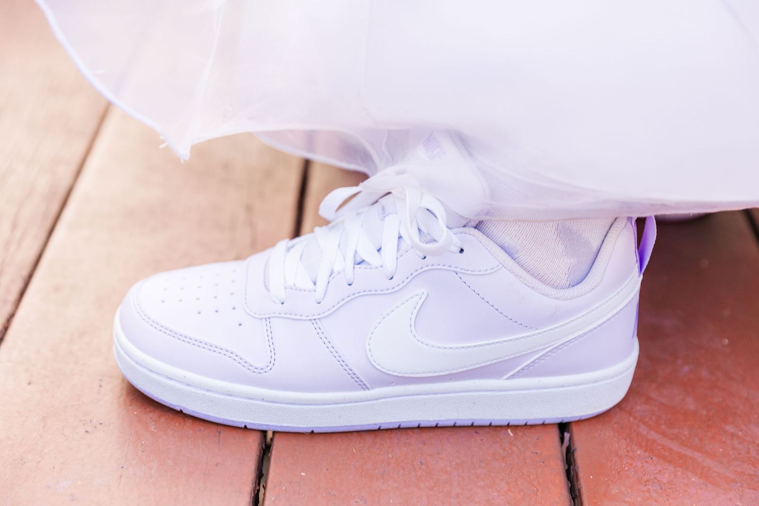 A white Nike sneaker positioned against wooden floorboards under flowing fabric.