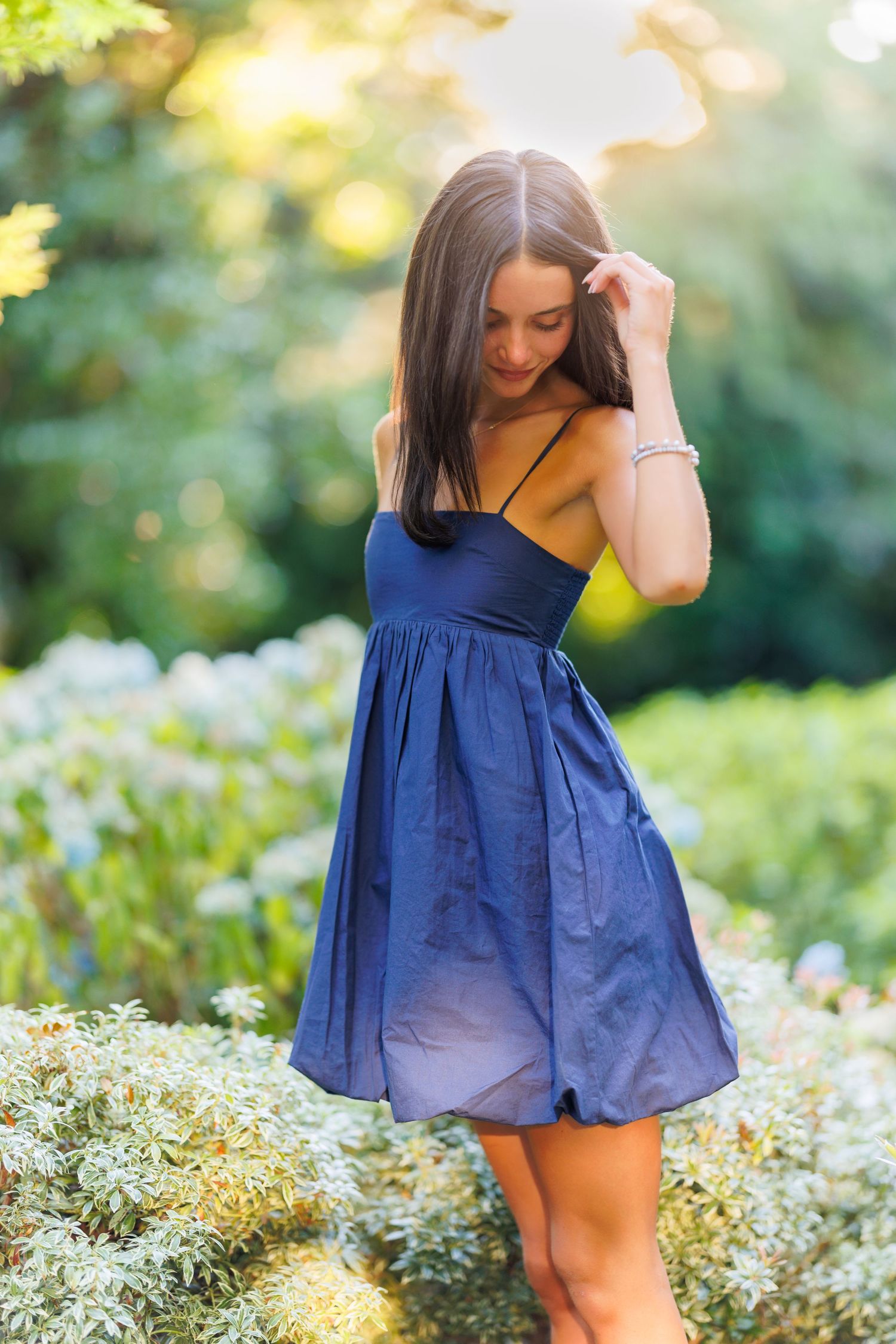 Summer portrait in navy blue dress among white flowers at sunset.