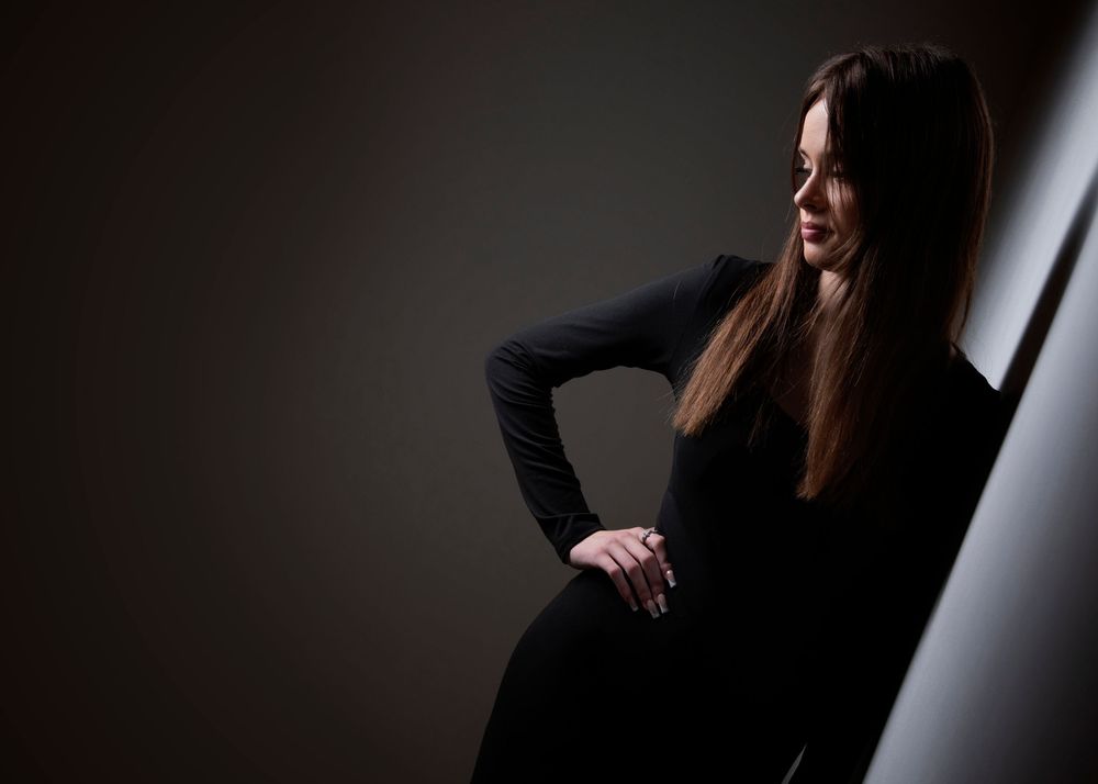 A silhouetted figure in a black outfit poses elegantly against a dramatic light and dark backdrop.