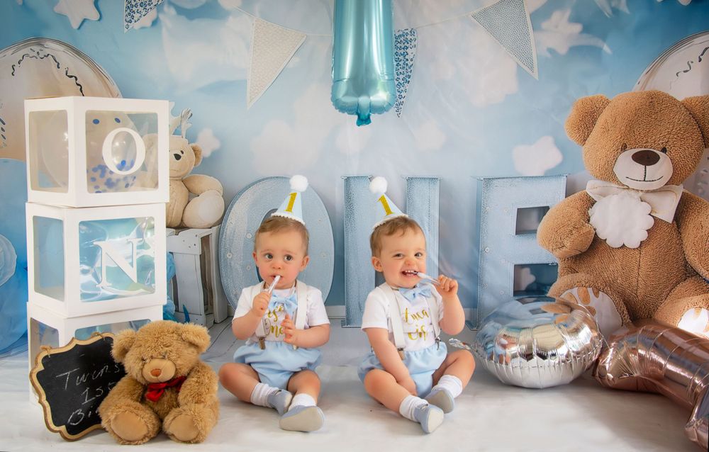 First birthday setup with blue balloon number 1, decorative boxes, and twin babies sitting together.
