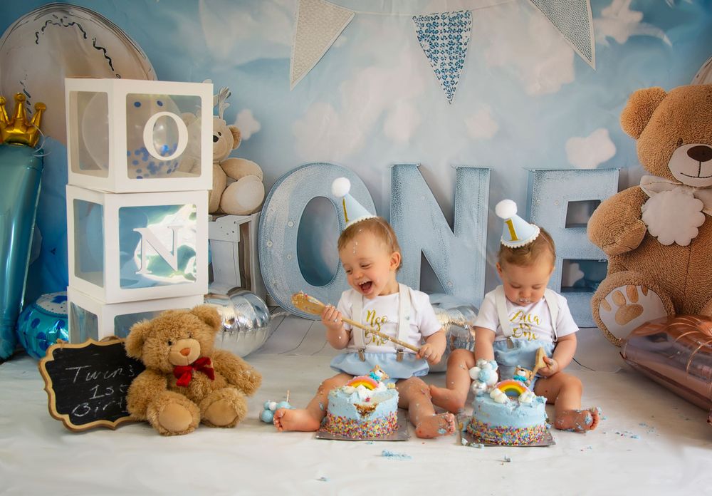First birthday photoshoot setup with blue and white decor, teddy bears, and twin babies in matching outfits.