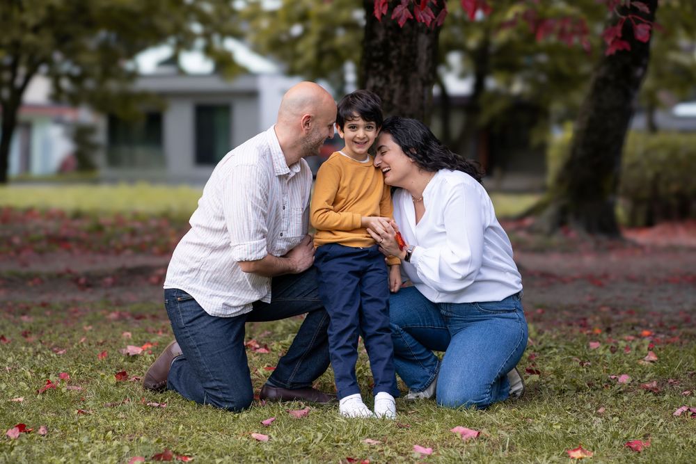 Family enjoying a tender moment together in a park during autumn with fallen leaves on the ground.