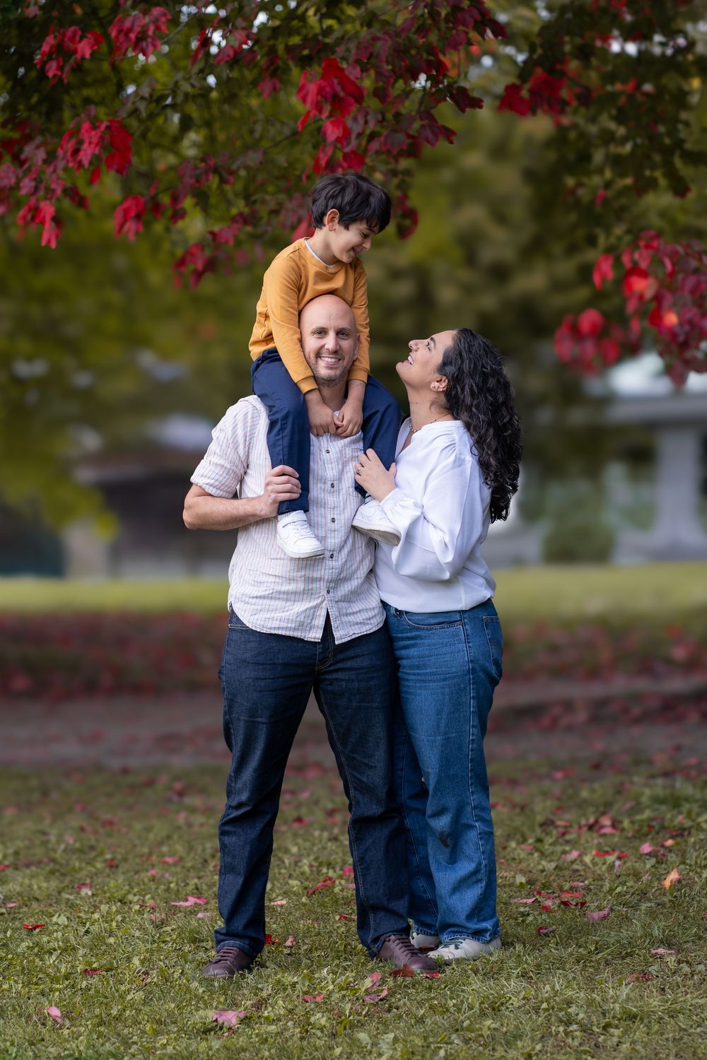 A family of three sharing a joyful moment under red autumn leaves.