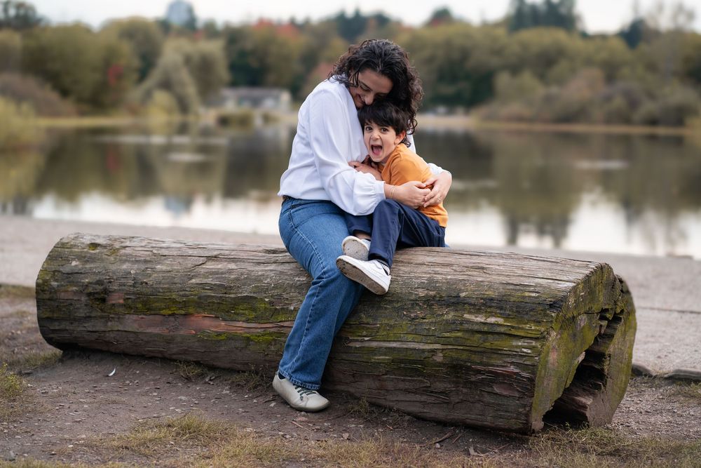 Parent and child sharing a quiet moment while sitting on a fallen log by a lake.