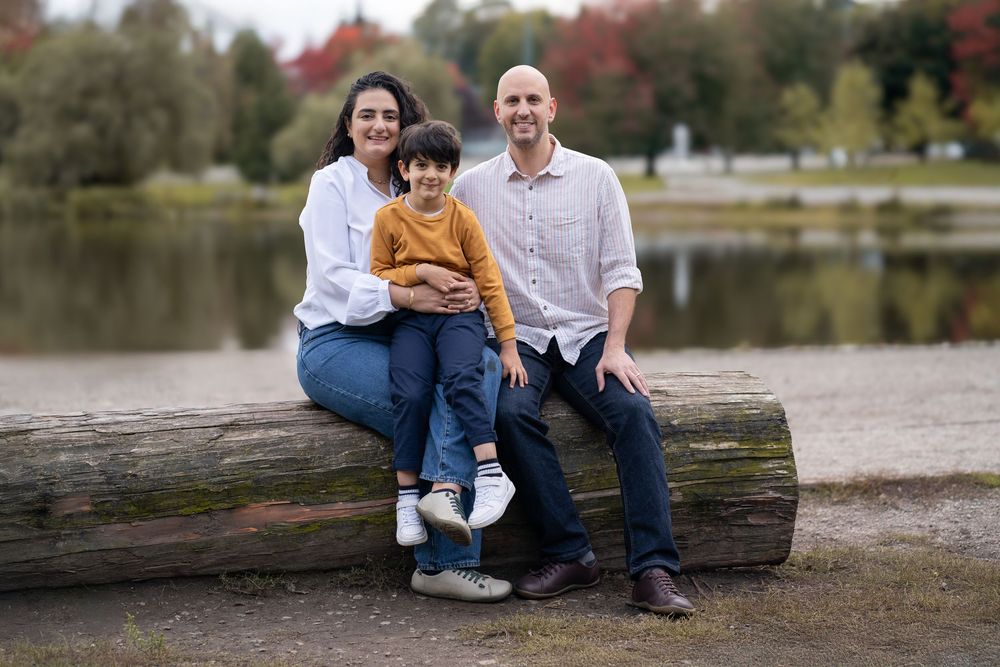 Family sitting together on a wooden log by a serene lake during fall season.