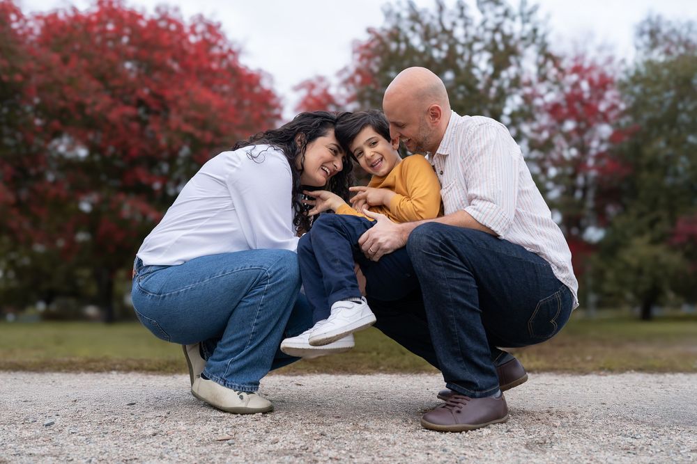 Family sharing an intimate moment outdoors surrounded by red autumn foliage.