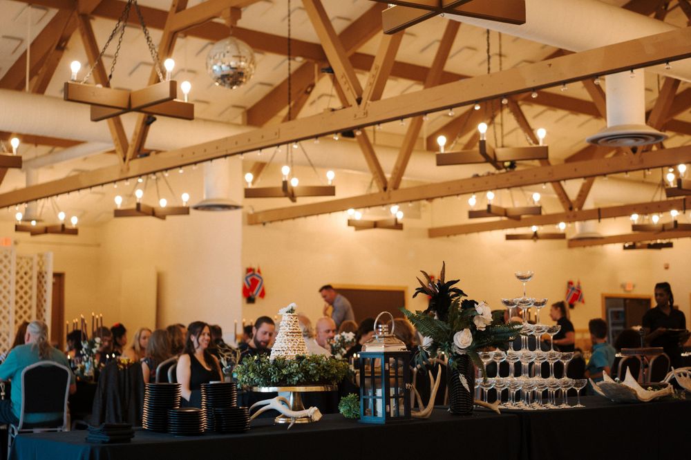 An elegant wedding reception venue with exposed wooden beams and hanging lights above guests seated at tables.