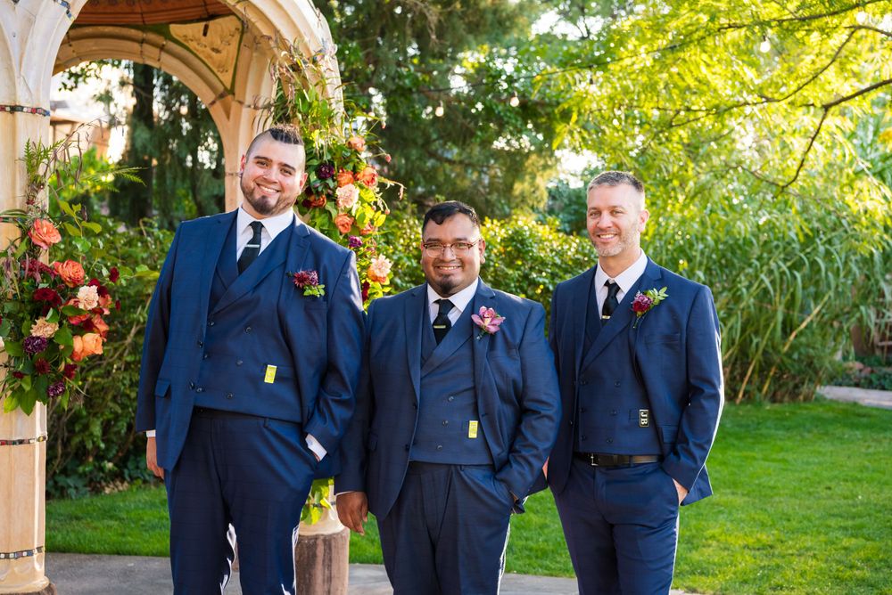 Three groomsmen in matching navy suits pose under an outdoor garden archway.