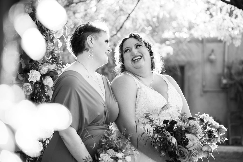 A candid black and white wedding moment shows the couple sharing laughter with floral bouquets.