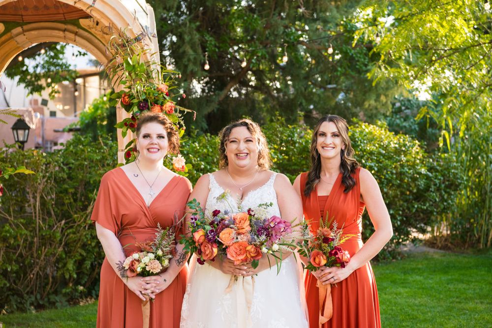 Wedding party with colorful bouquets poses together under garden archway.