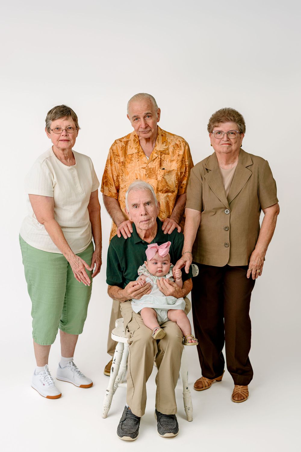 Multi-generational family portrait with baby in studio setting on white background.