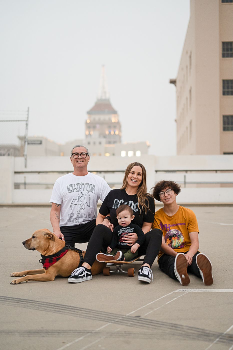 Family group with dog sitting on urban rooftop with building dome visible in background.