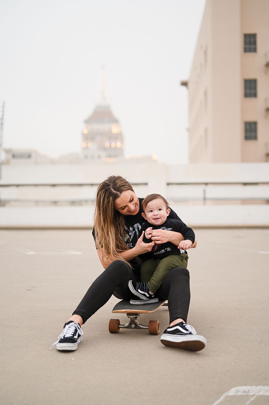 Parent and child sharing moment while sitting on skateboard on urban rooftop.