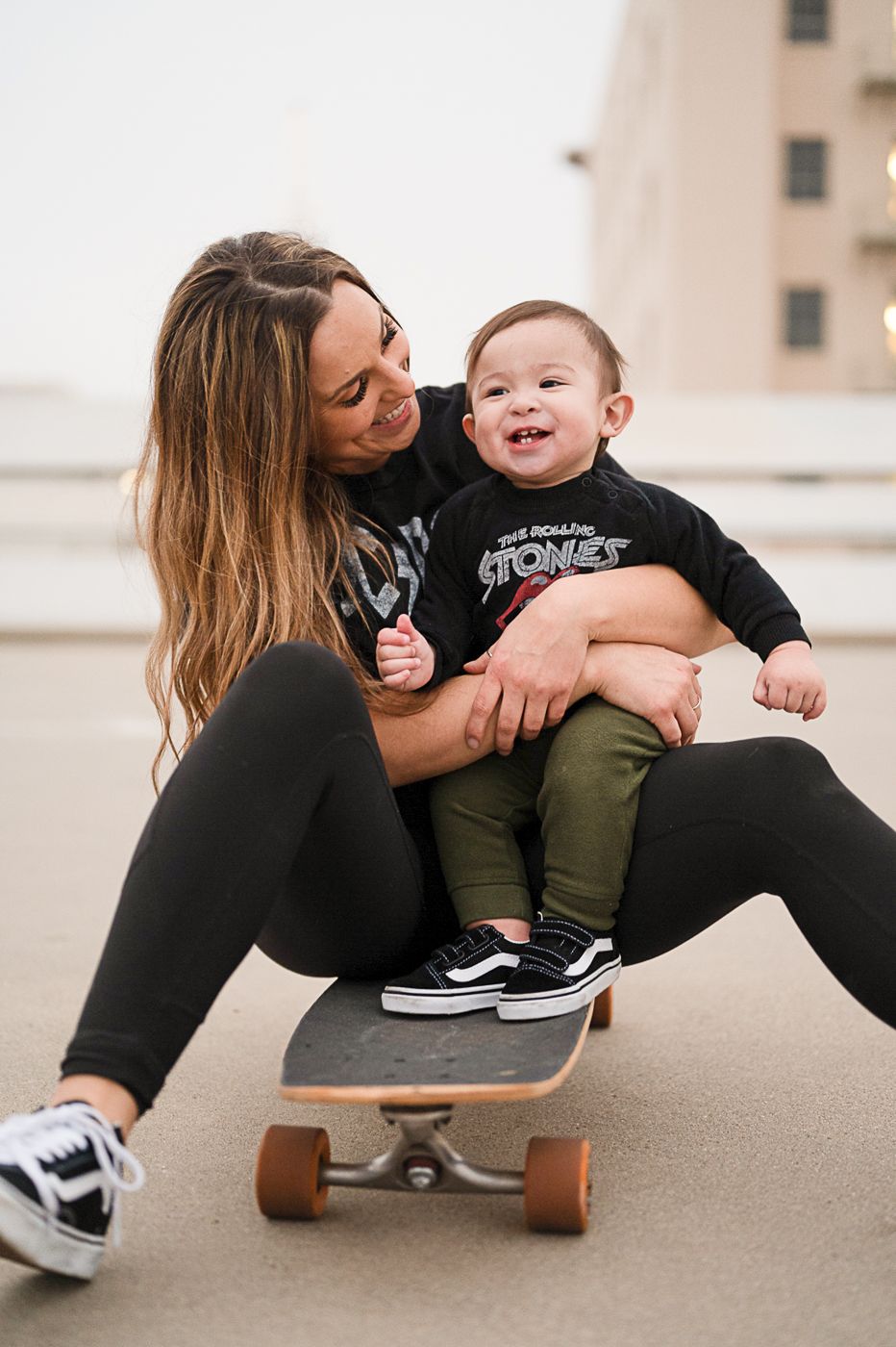 Parent and child share joyful moment while sitting on skateboard.