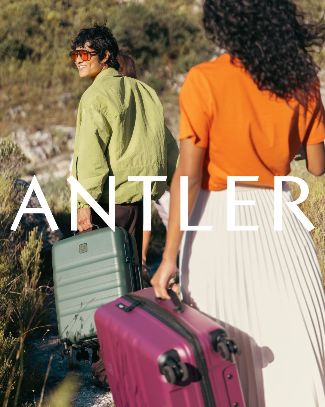 Two people carrying Antler suitcases while hiking on mountain trail.