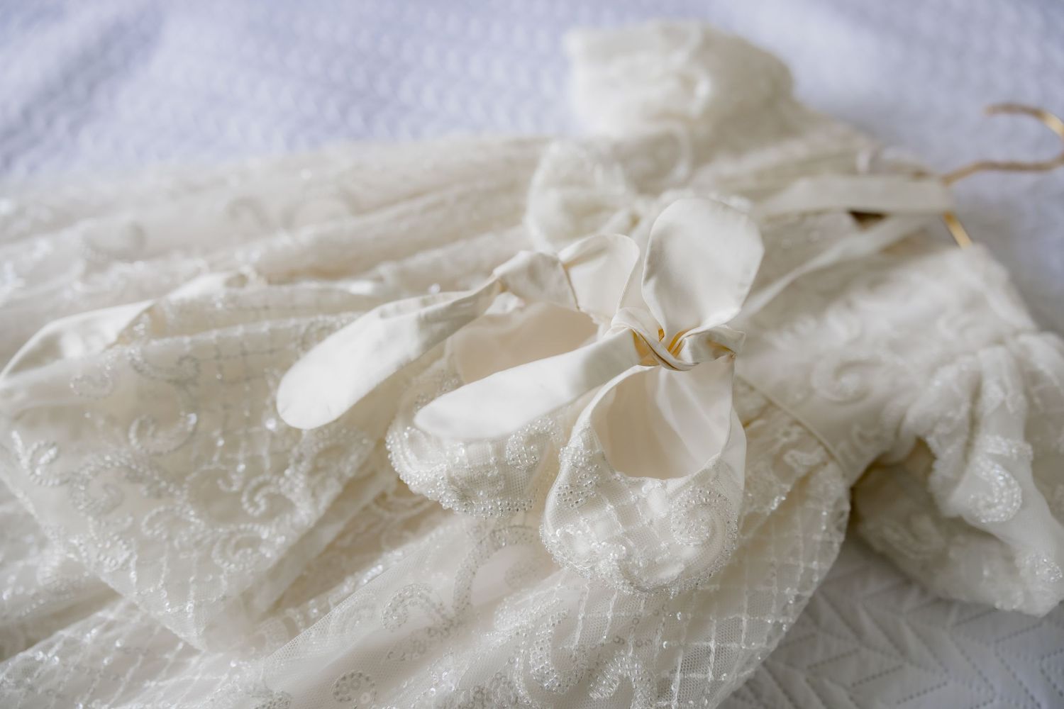 Close-up detail of white lace christening gown with bow embellishment.