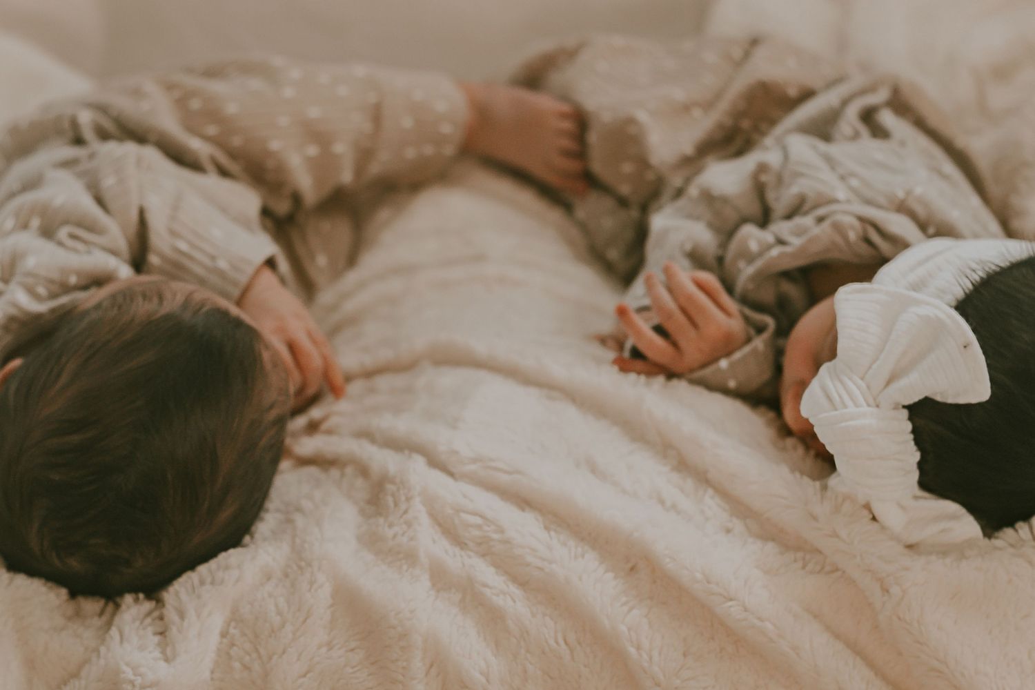 Two young children sleeping peacefully together wrapped in a soft beige blanket on a cozy bed.