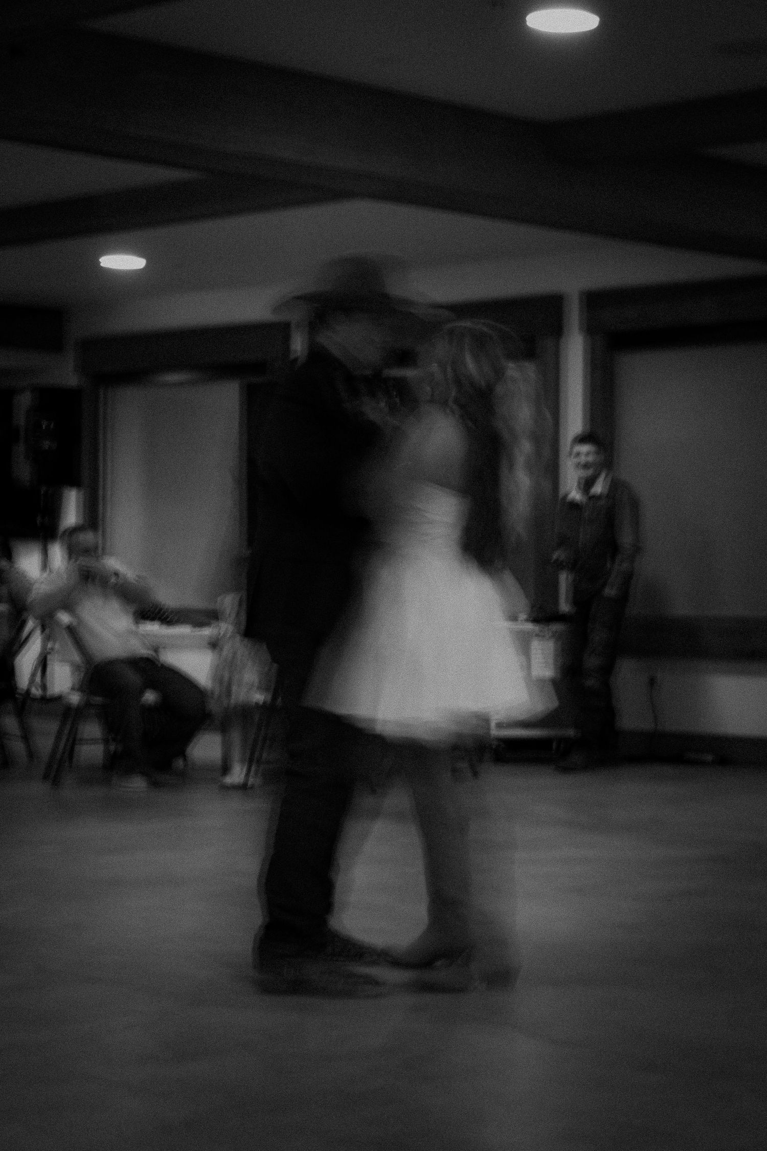 Black and white photo of a couple sharing a romantic dance at a formal event while guests watch in the background.